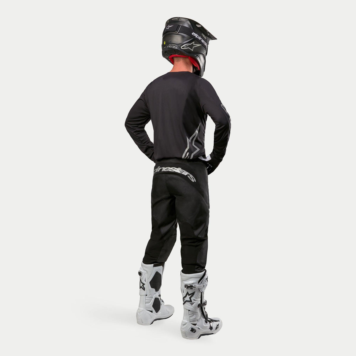 Alpinestars 2024 Fluid Graphite Pants, Motocross Pants, Black and Silver, rear view on a rider wearing a black jersey, black helmet, and white and black boots, featuring silver branding on the lower back and a durable poly-fabric construction for off-road racing