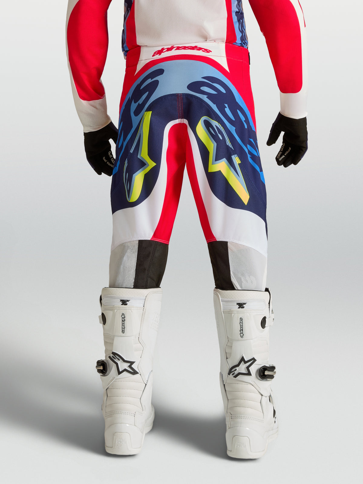 Alpinestars Supertech Dyna bukser til ungdom, professionelle motocrossbukser i rød og blå med hvid og gul grafik, set bagfra på model med hvide motorcykelstøvler, avanceret stretch rip-stop konstruktion.