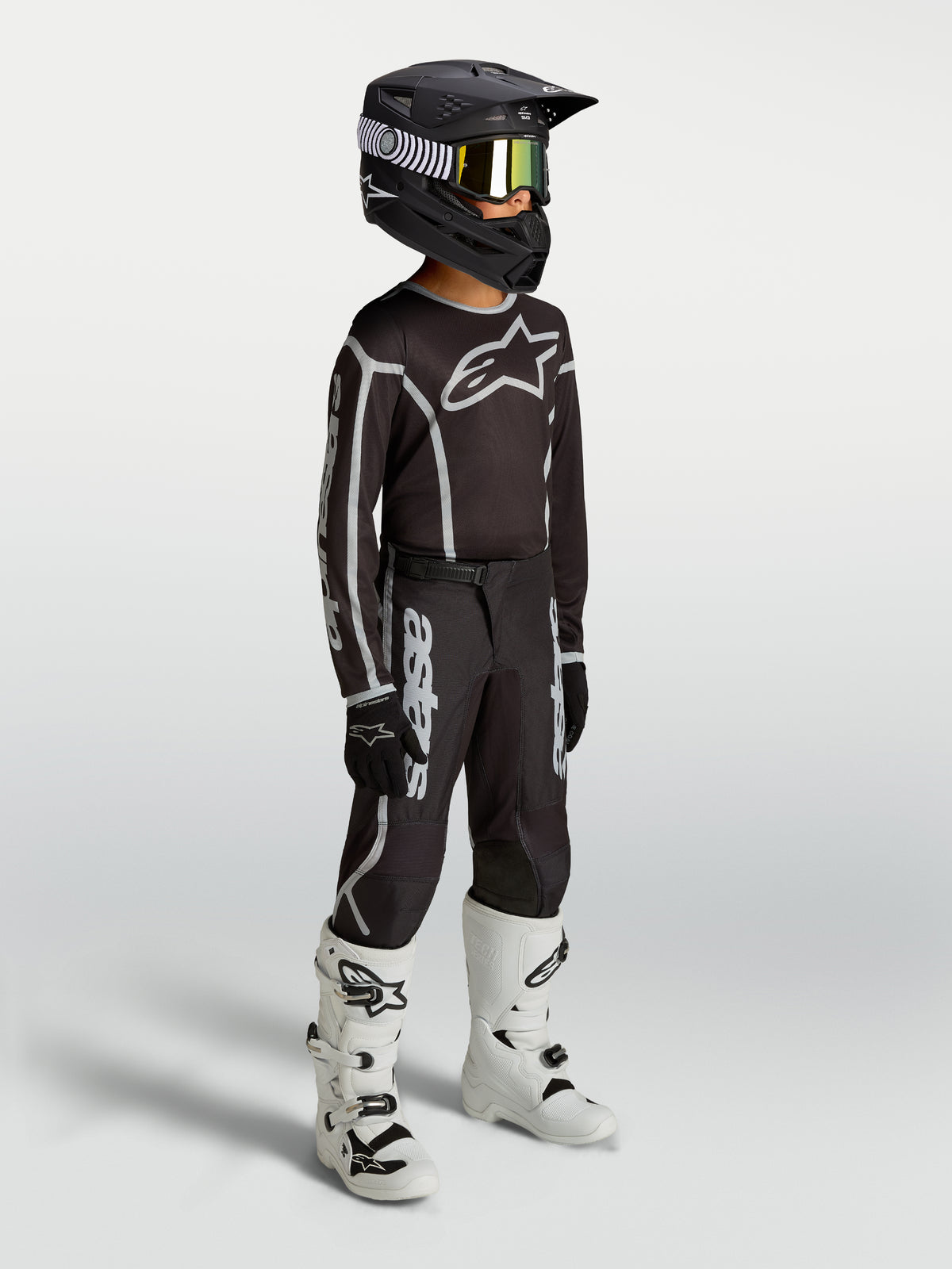 Alpinestars Youth Fluid Apex V2 Pants, black and silver motocross gear shown on-model with jersey, helmet, and white boots.