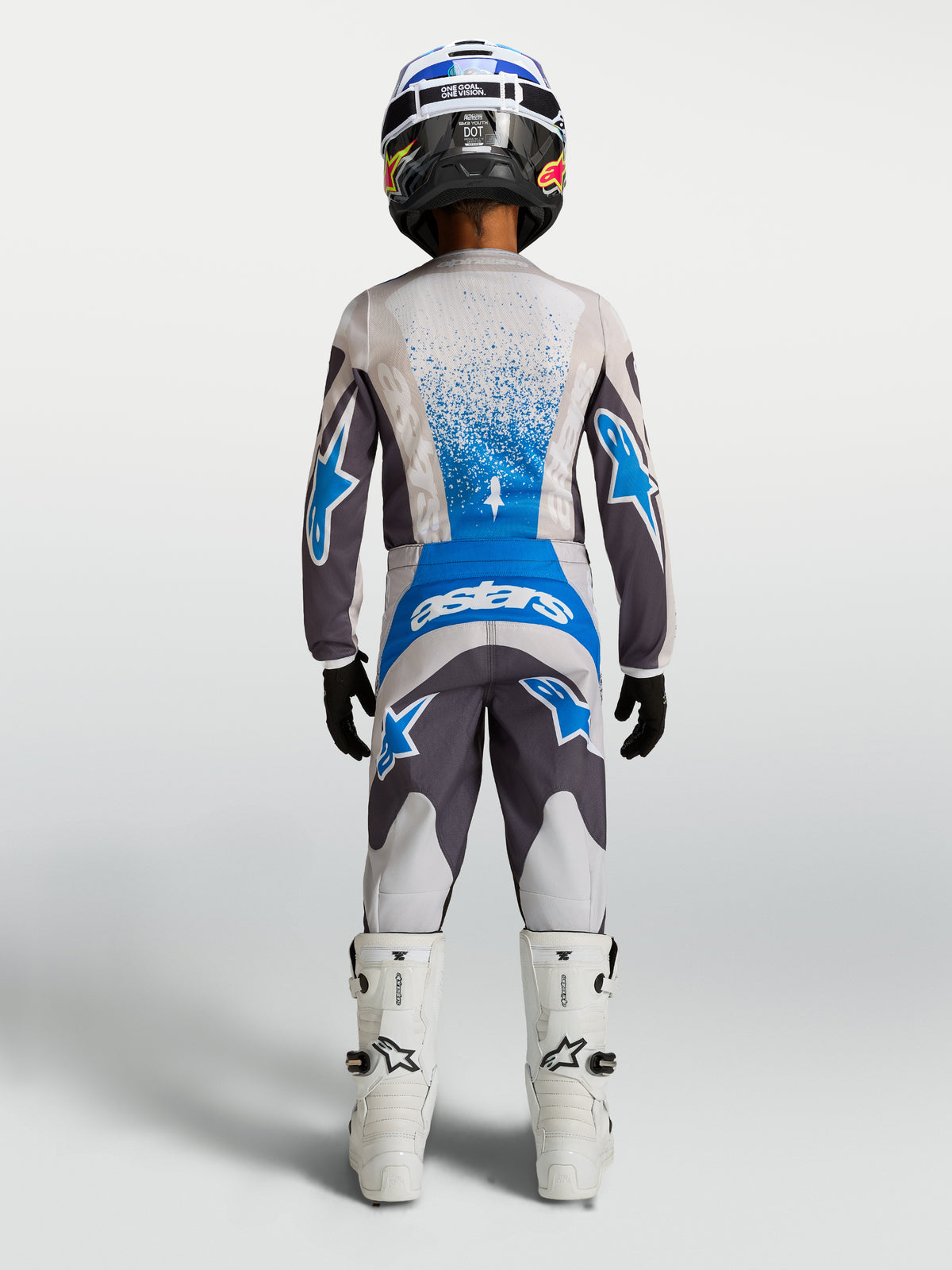 Alpinestars 2027 Fluid Drag Bukser Ungdom, grå og blå motocrossbukser til terrænkørsel, set bagfra på model med matchende trøje og hvide motorcykelstøvler.