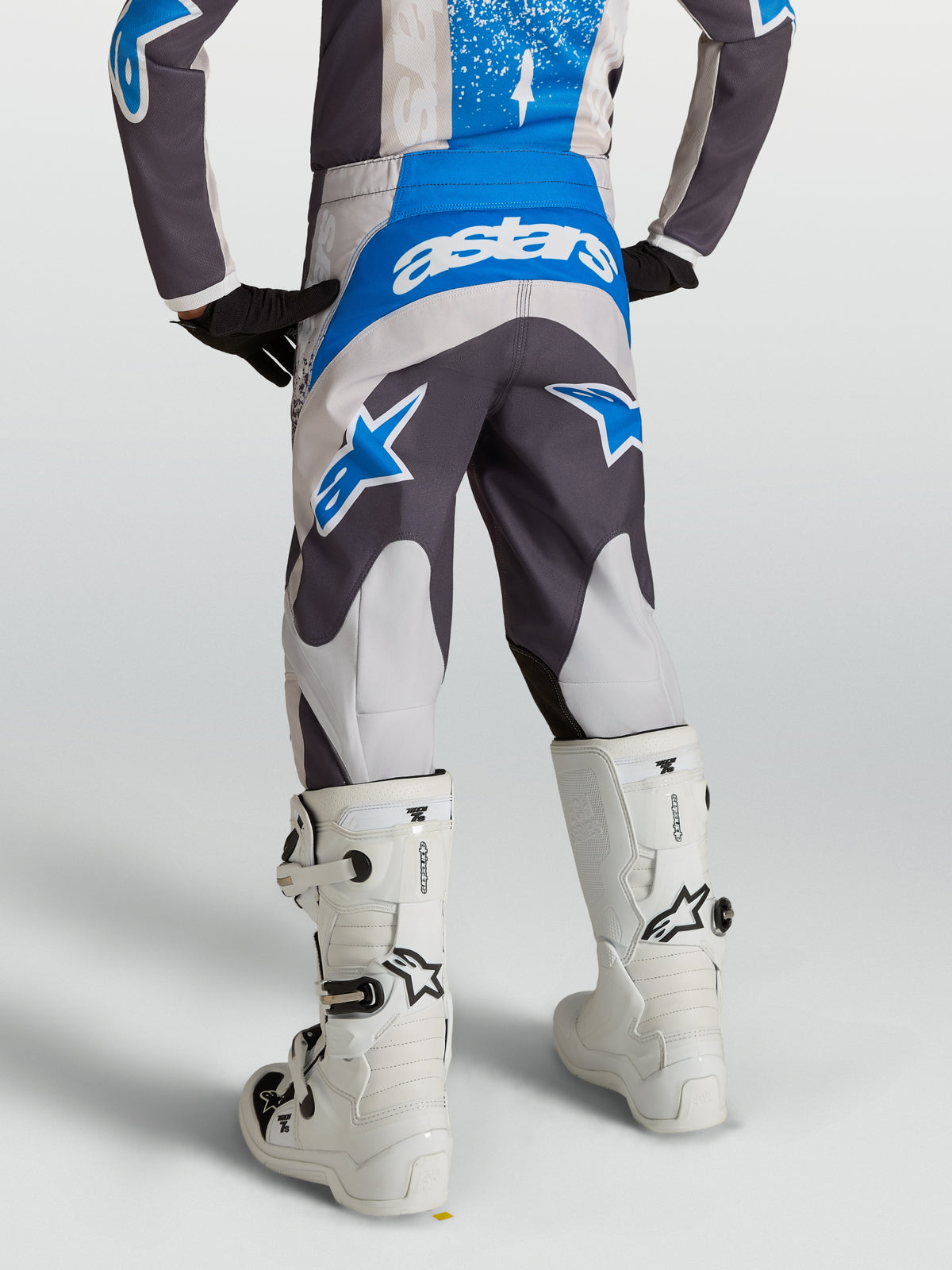 Alpinestars 2027 Fluid Drag motocrossbukser til unge, grå og blå, set bagfra på en rytter med hvide støvler.