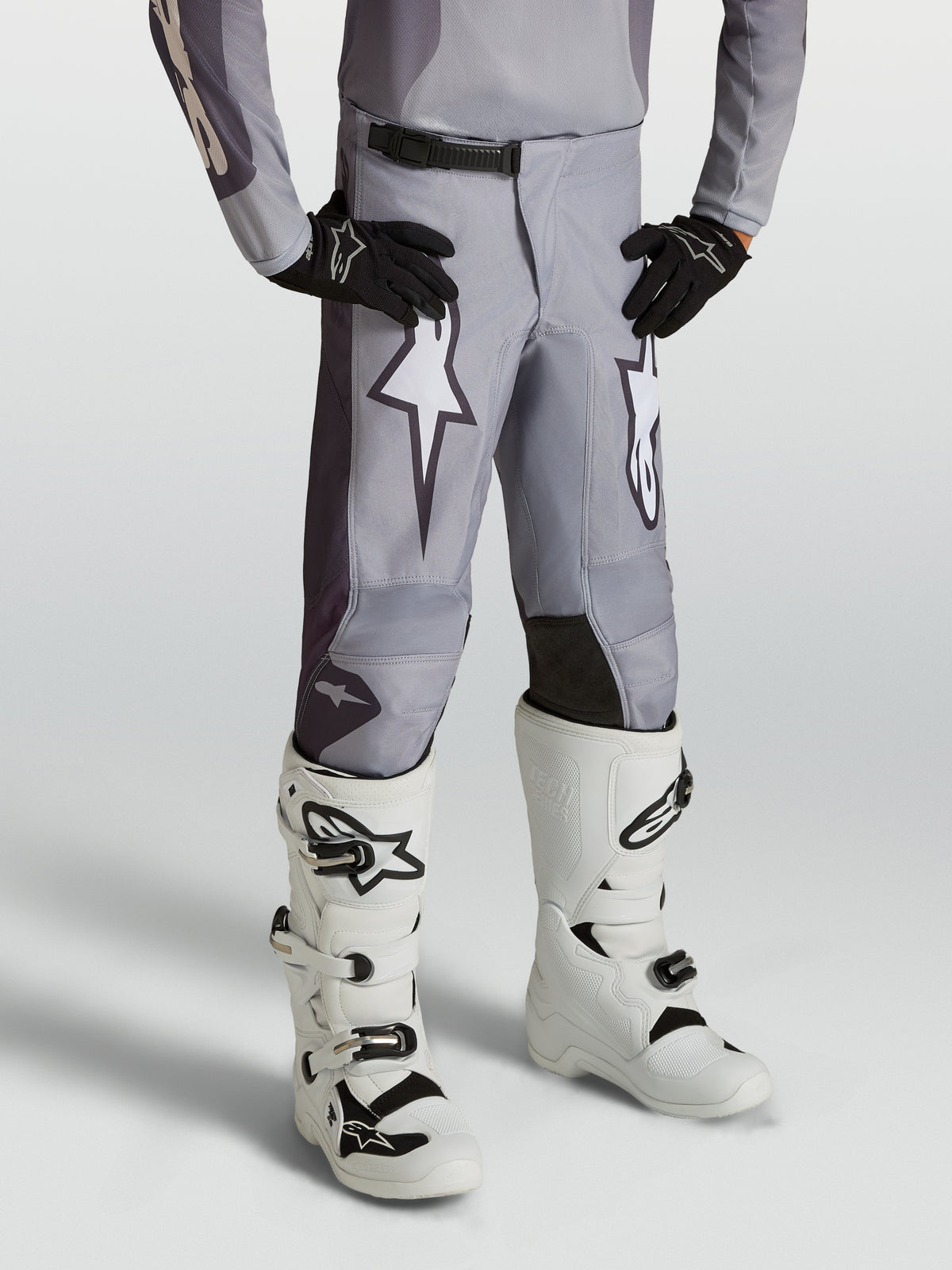Alpinestars 2027 Fluid Amber bukser ungdom, sandgrå motocrossbukser med hvid stjernegrafik og forstærkede paneler, vist på en model med hvide støvler.