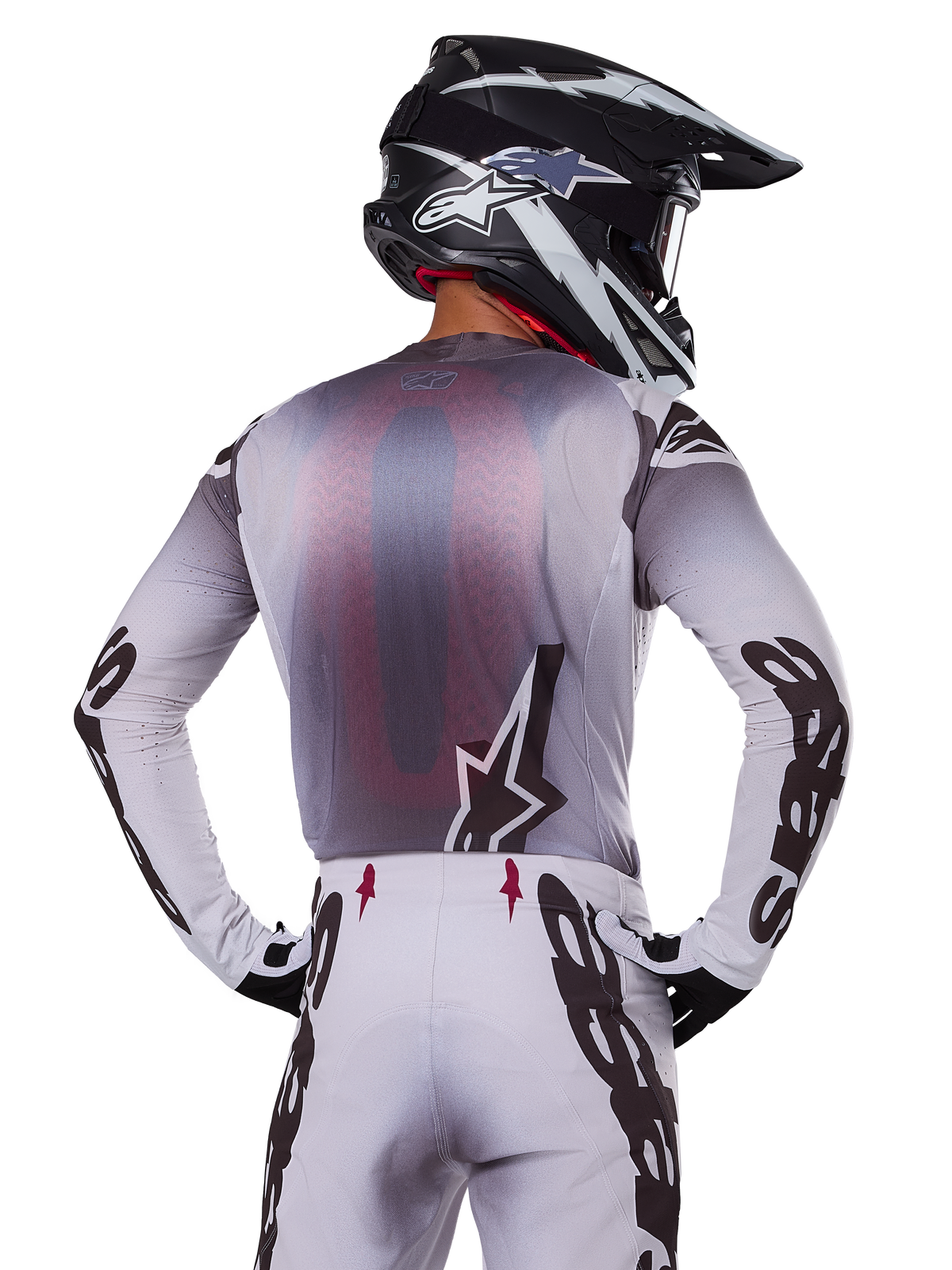 Alpinestars 2025 Supertech Maker udstyrssæt, motocross-rytter set bagfra, hvid og grå jersey med stor sort branding på ærmerne og stjernelogo, matchende hvide bukser med sort grafik, sort og hvid hjelm, professionelt terrænkørselsudstyr