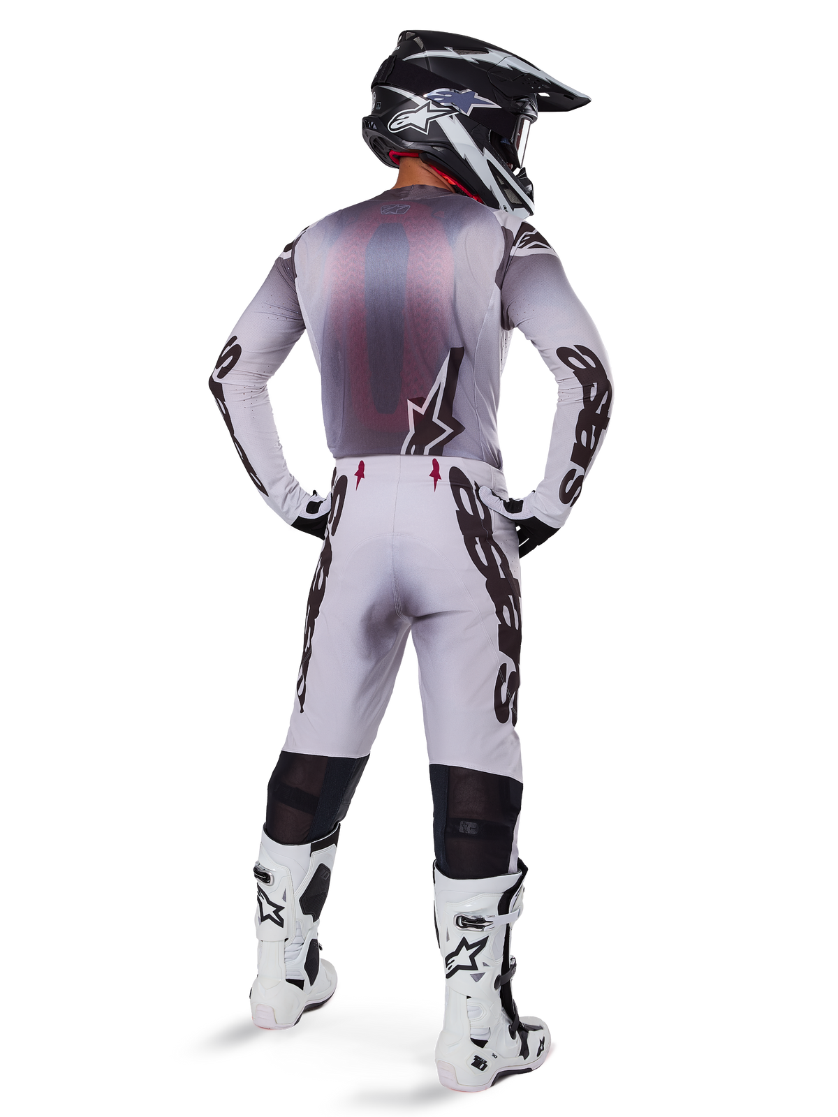 Motocrosskører set bagfra iført 2025 Supertech Maker-udstyrssættet i hvid, med en grå og hvid jersey med sort Alpinestars-branding, matchende motocrossbukser, hvide og sorte støvler og en sort hjelm, koordineret off-road racersæt
