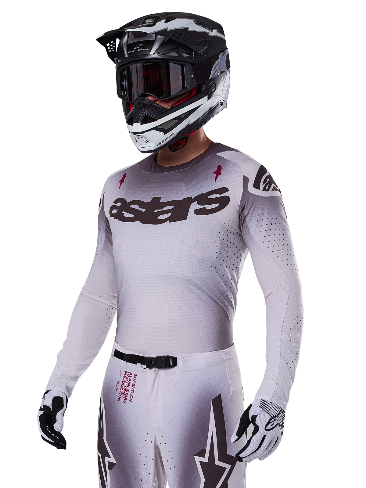 Alpinestars 2025 Supertech Maker-udstyrssæt i hvid, motocross-kører med en grå gradueret jersey, sort astars-logo og laserskårne perforeringer, matchende bukser med magnetisk spænde og stjernegrafik, sort og hvid hjelm og handsker, komplet off-road racing-look.