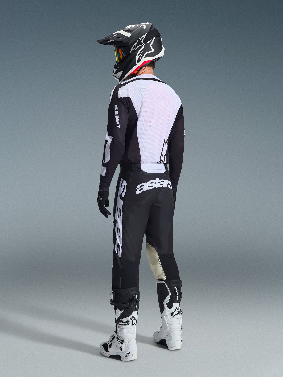 Motocross rider from a rear view wearing the 2026 Racer Air Riway Jersey in Black and White, showcasing the large white mesh back panel for airflow, paired with black pants, black and white helmet, and white racing boots, complete professional gear for off-road performance.