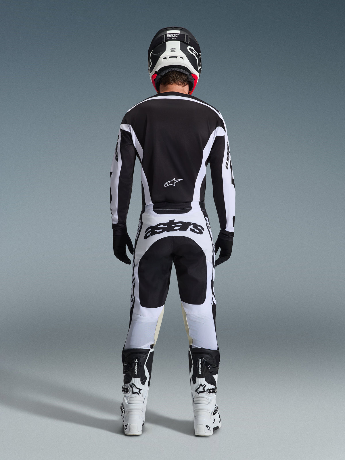 Alpinestars 2026 Racer Riway Gear Set, set bagfra af en motocrosskører i sort og hvidt, sort jersey med hvide detaljer, hvide bukser med markant 'astars' branding på sædet, sort hjelm, hvide støvler og sorte handsker, komplet professionelt udstyr til terrænkørsel.