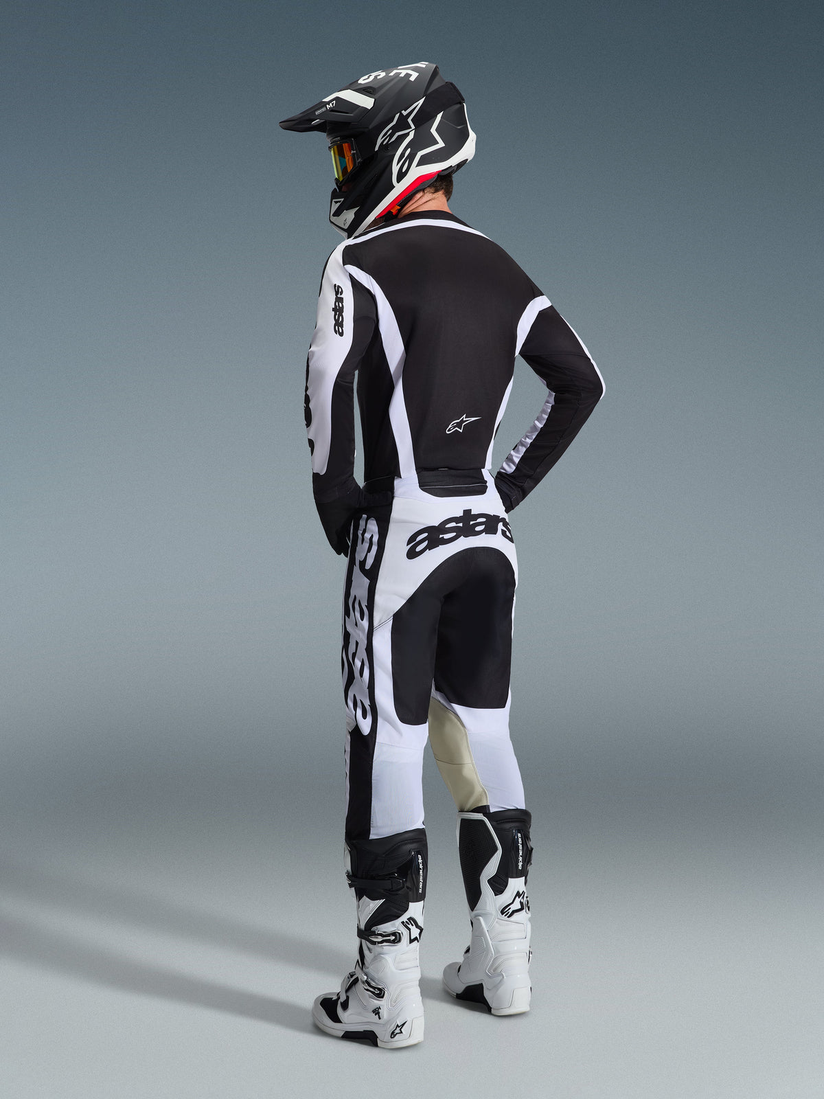Motocrosskører set bagfra iført Alpinestars 2026 Racer Riway-udstyrssæt i sort og hvid, med en matchende sort hjelm og hvide motocrossstøvler, strømlinet højtydende design til terrænkørsel