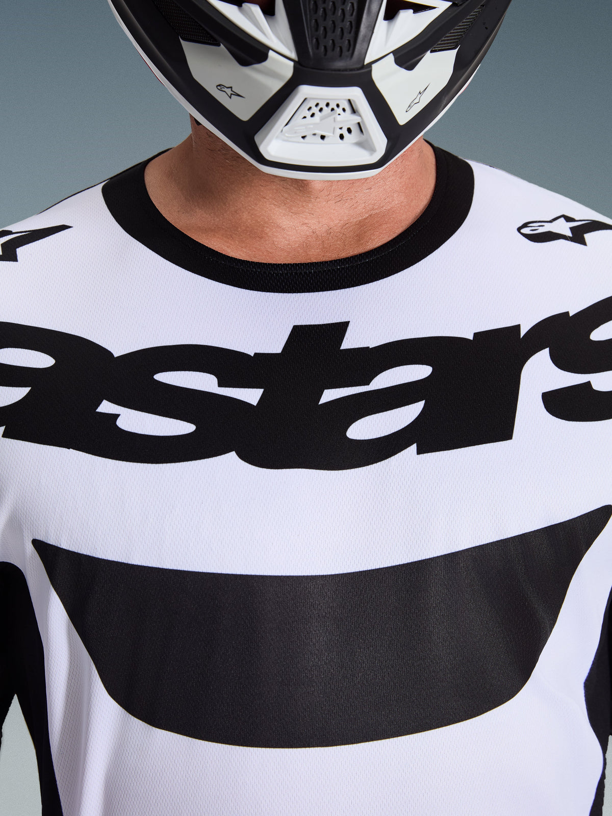 Nærbillede af en kører iført Alpinestars 2026 Racer Riway Jersey i hvid og sort, med markant 'astars'-branding over brystet og en sort rund hals, kombineret med en matchende motocross-hjelm.