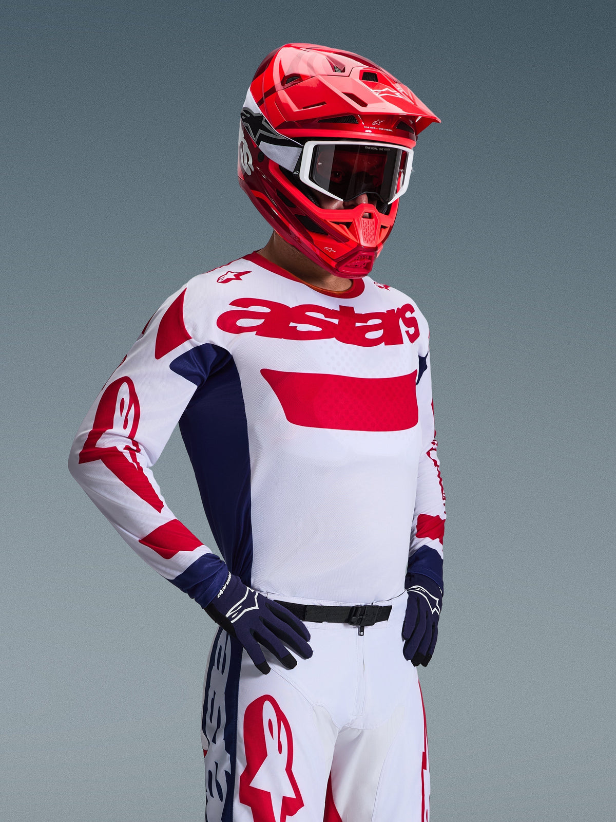Motocross-kører iført Alpinestars 2026 Racer Riway Jersey i hvid, blå og rød, matchende off-road bukser, klar rød hjelm med hvide goggles og mørkeblå handsker, koordineret højtydende udstyrssæt til motocross