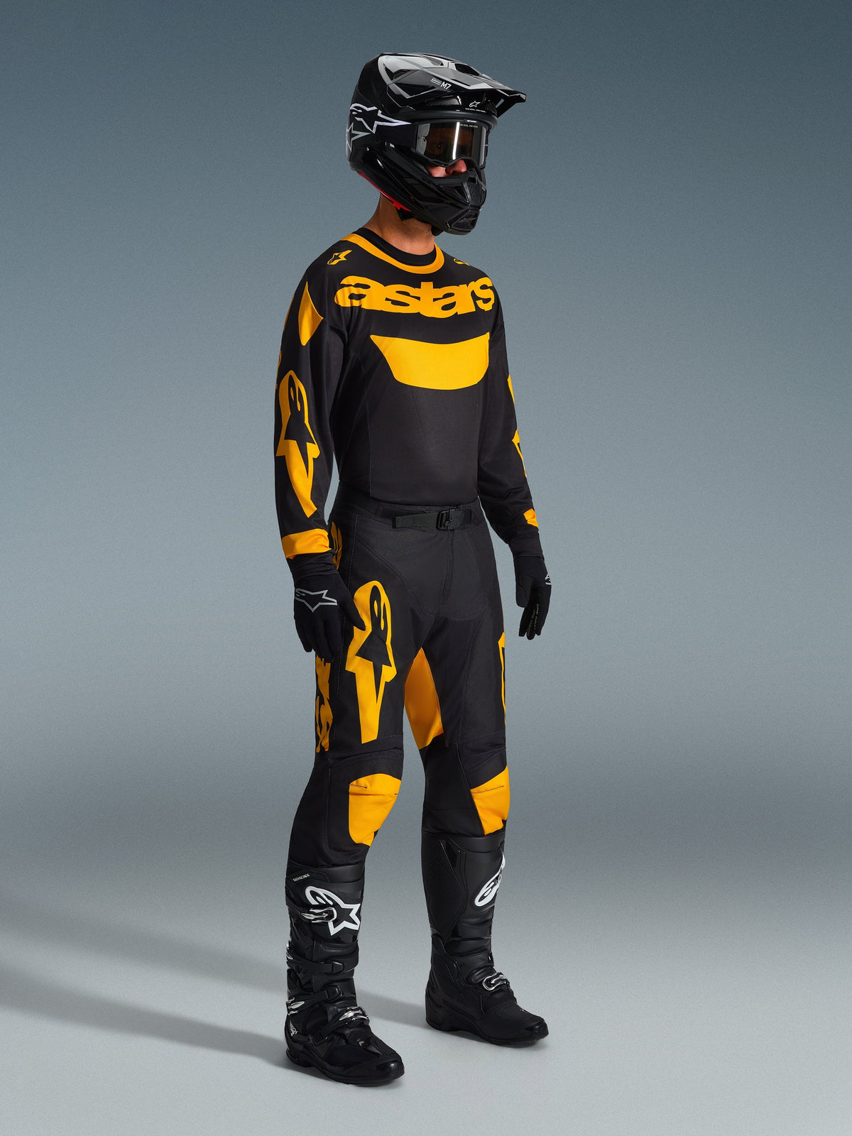 Motocross-kører iført 2026 Racer Riway-trøje i gul og sort, komplet racersæt med matchende bukser, sort hjelm, handsker og støvler, designet til off-road performance med markant Alpinestars-grafik.