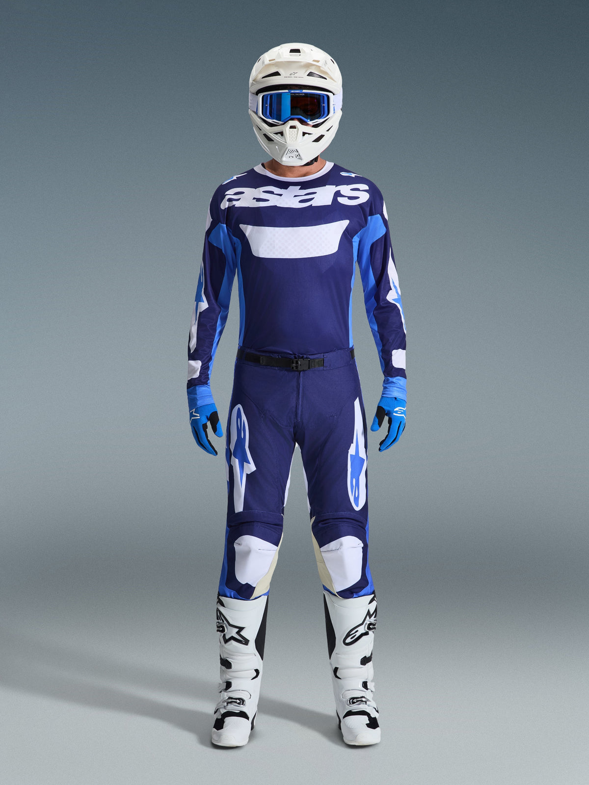 Alpinestars motocross-kører i komplet racerudstyr, 2026 Racer Riway-trøje i UCLA Blue og hvid med navyblå paneler og 'astars'-branding på brystet, matchende blå og hvide bukser, hvid hjelm med blå briller, hvide og sorte støvler, blå handsker, koordineret motocross-racersæt