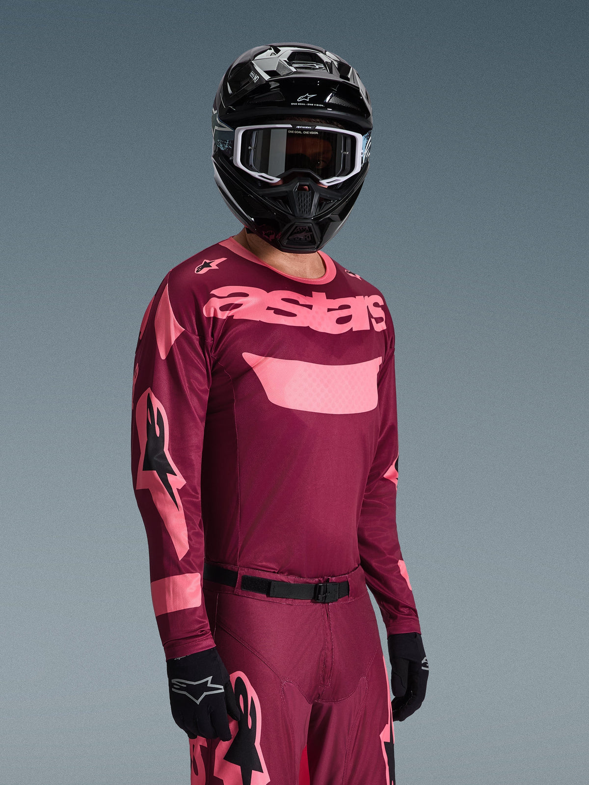 Motocross-kører iført Alpinestars 2026 Racer Riway Jersey i Dark Red Coral med matchende bukser, med koralfarvet 'astars'-branding på brystet, kombineret med en sort hjelm og sorte handsker, koordineret sæt til off-road racing.