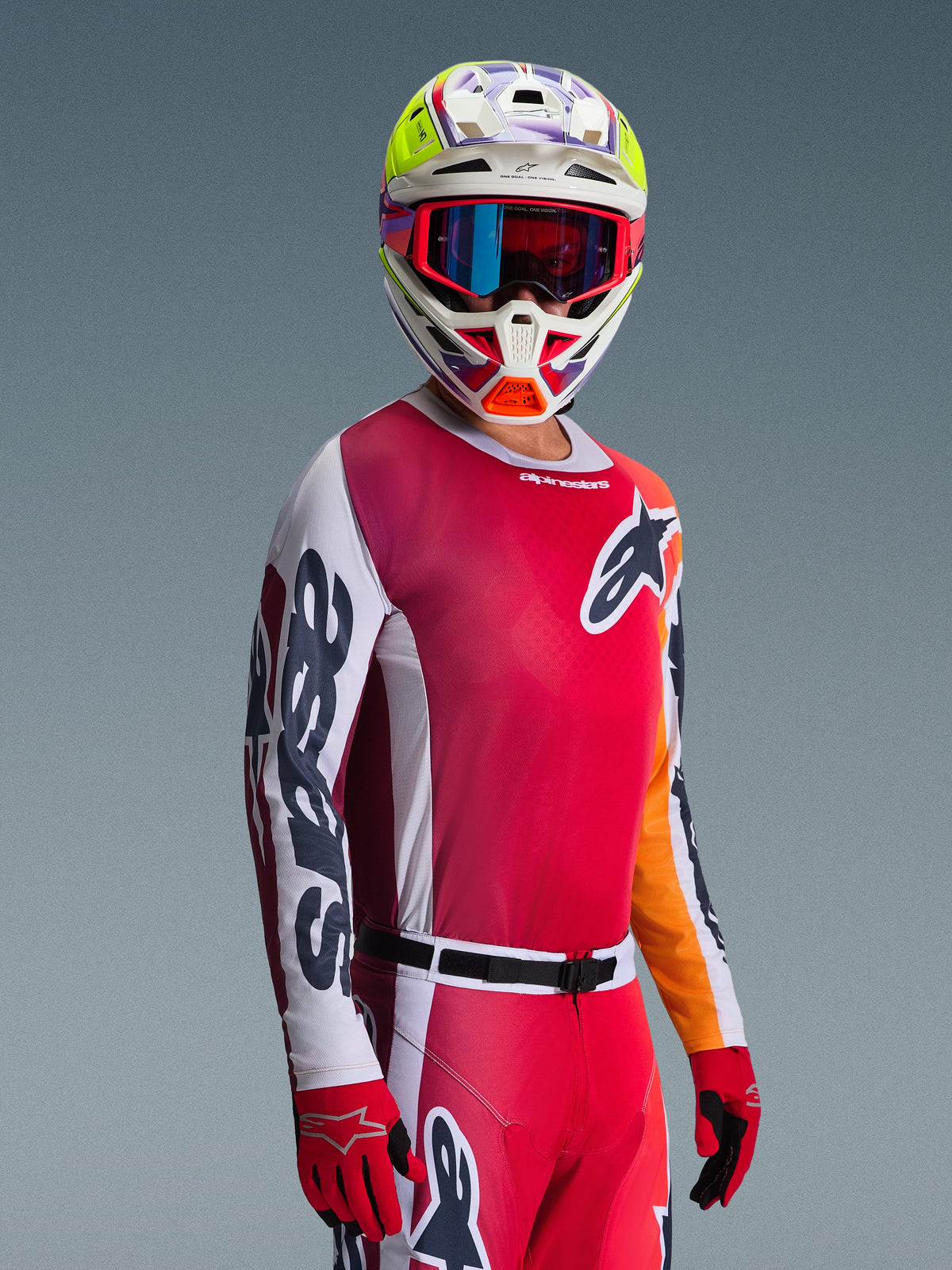 Alpinestars 2026 Racer Portl Gear Set, motocrosskører iført en rød jersey med lyserøde toner og hvide ærmer, matchende røde bukser, hvid hjelm med livlige gule og lilla detaljer, røde goggles med blå iriserende linser og røde handsker, professionelt racingoutfit til motocross.