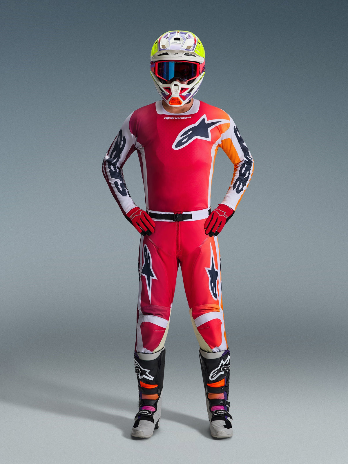 Motocross-kører iført Alpinestars 2026 Racer Portl trøje i rød, med hvide og orange grafiske detaljer, matchende motocross-bukser, røde handsker, farverig racerhjelm med goggles og sort-hvide tekniske støvler, komplet off-road racerudstyr