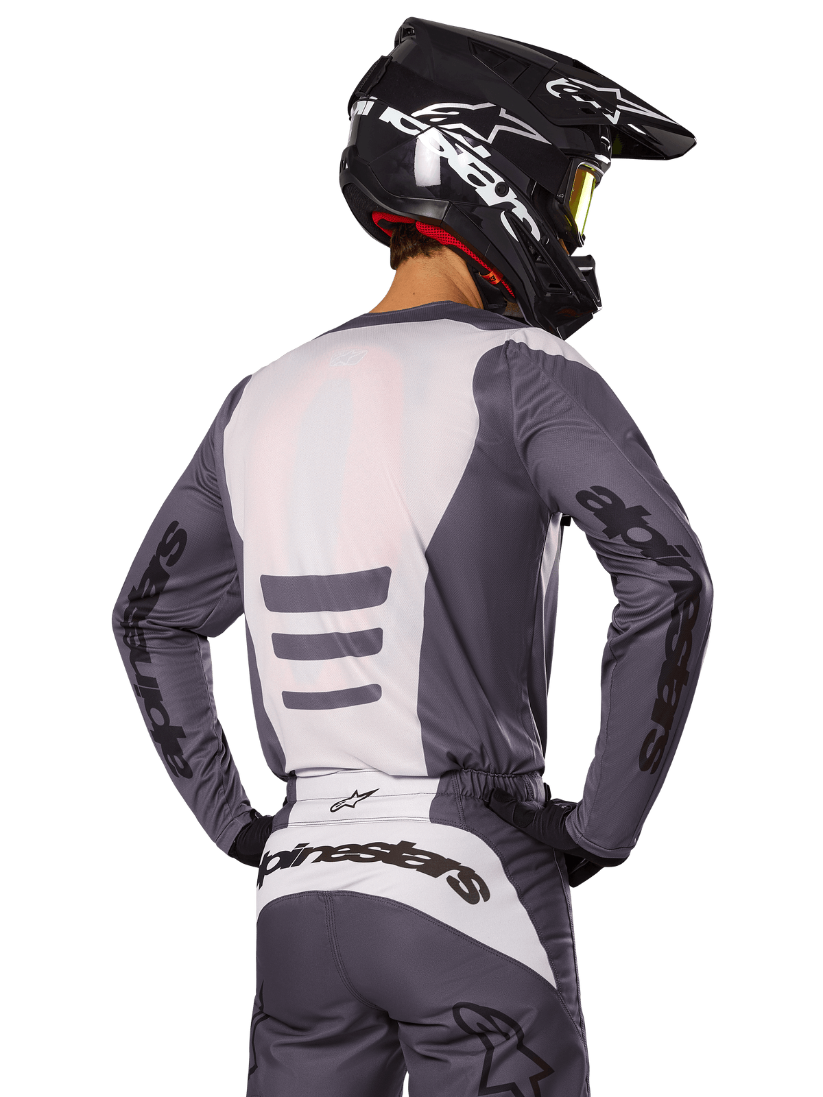 Motocrossrytter set bagfra iført Alpinestars 2025 Fluid Haul-udstyrssæt, grå og hvid trøje og bukser, sort hjelm med hvid grafik, gule goggles, koordineret motocross-raceroutfit