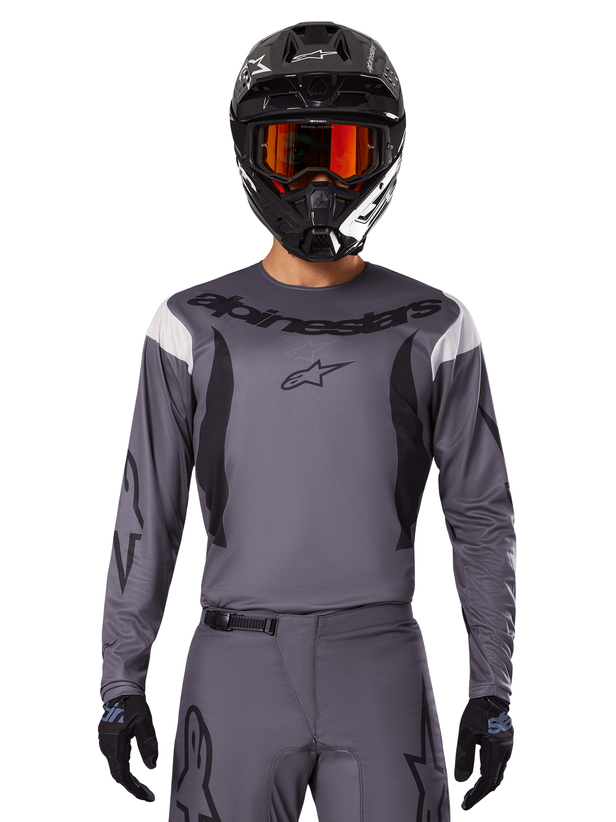 Motocross-rytter iført Alpinestars 2025 Fluid Haul Jersey og udstyrssæt, grå med sorte og hvide detaljer, langærmet design med markant branding, sort hjelm med orange goggles og sorte handsker, koordineret outfit til off-road racing