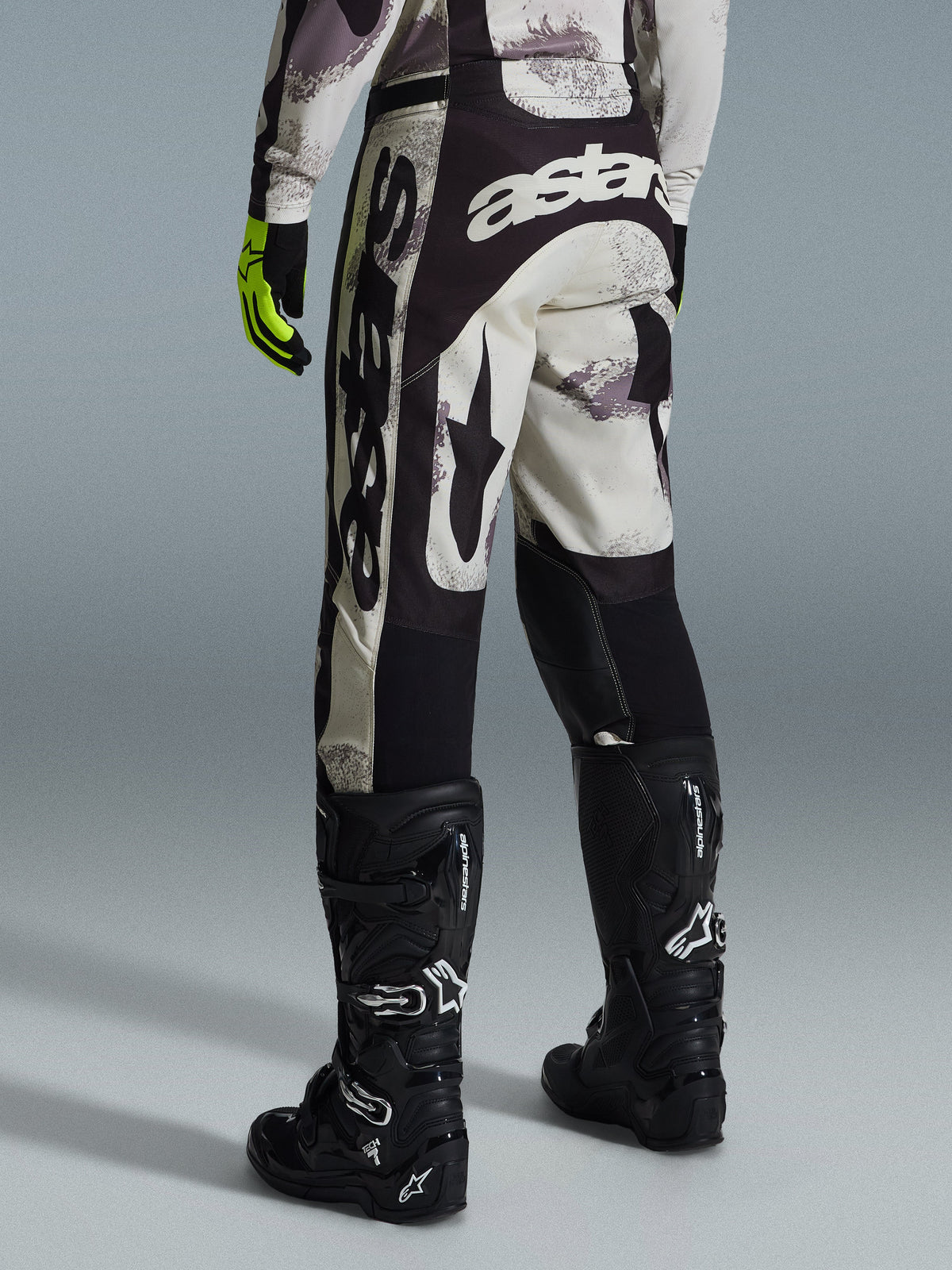 Alpinestars 2026 Racer Lahnd bukser, motocross-bukser, sand camo og grå, set bagfra med markant hvid branding på sædet og benene, kombineret med sorte motocross-støvler og gule handsker, professionelt off-road racingudstyr