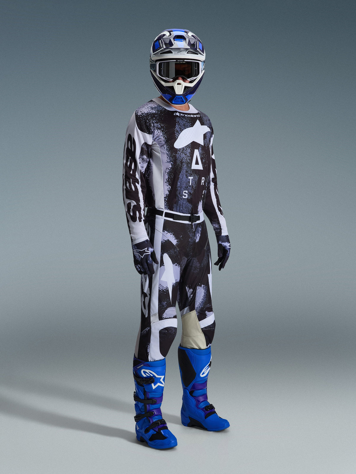 Alpinestars 2026 Racer Lahnd Gear Set, motocross rider wearing a black and white patterned jersey and pants with an abstract weathered design, featuring large white Alpinestars branding, paired with vibrant blue and purple boots and a blue and white helmet, complete professional off-road racing outfit.