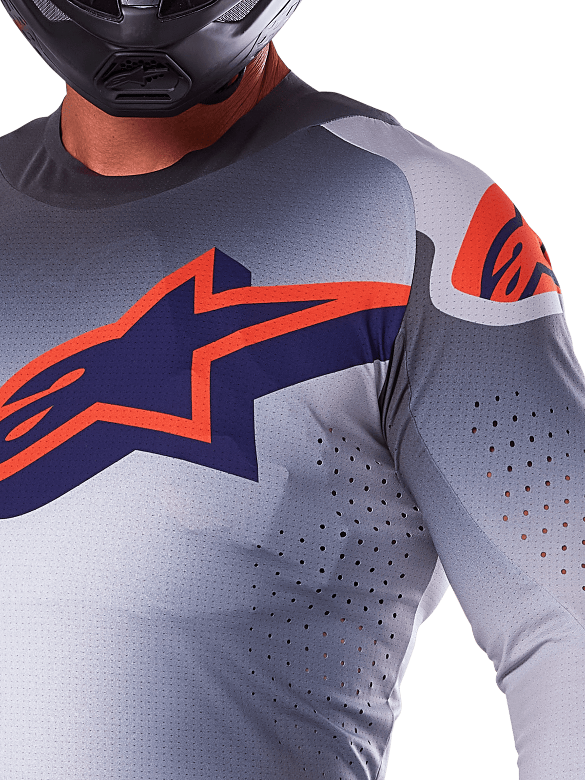 Nærbillede af en kører iført Alpinestars 2025 Supertech Lipan jersey, motocross-trøje, grå og orange fluo, med et stort orange Alpinestars-logo på brystet, laser-skårne ventilationshuller og en sort hjelm, professionelt racerudstyr