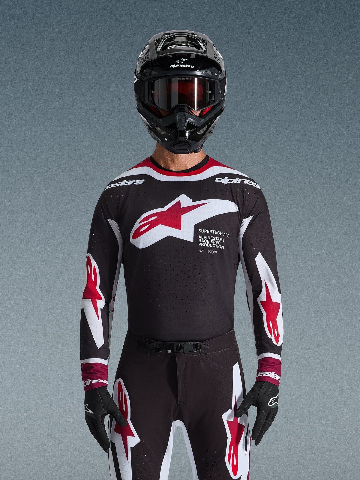 Alpinestars 2026 Supertech AFD Vista Jersey, motocross-trøje i sort, rød og hvid, vist på en kører med sort hjelm, goggles og handsker, med et stort logo på brystet og 'SUPERTECH AFD'-branding, professionelt racingudstyr til terrænkørsel