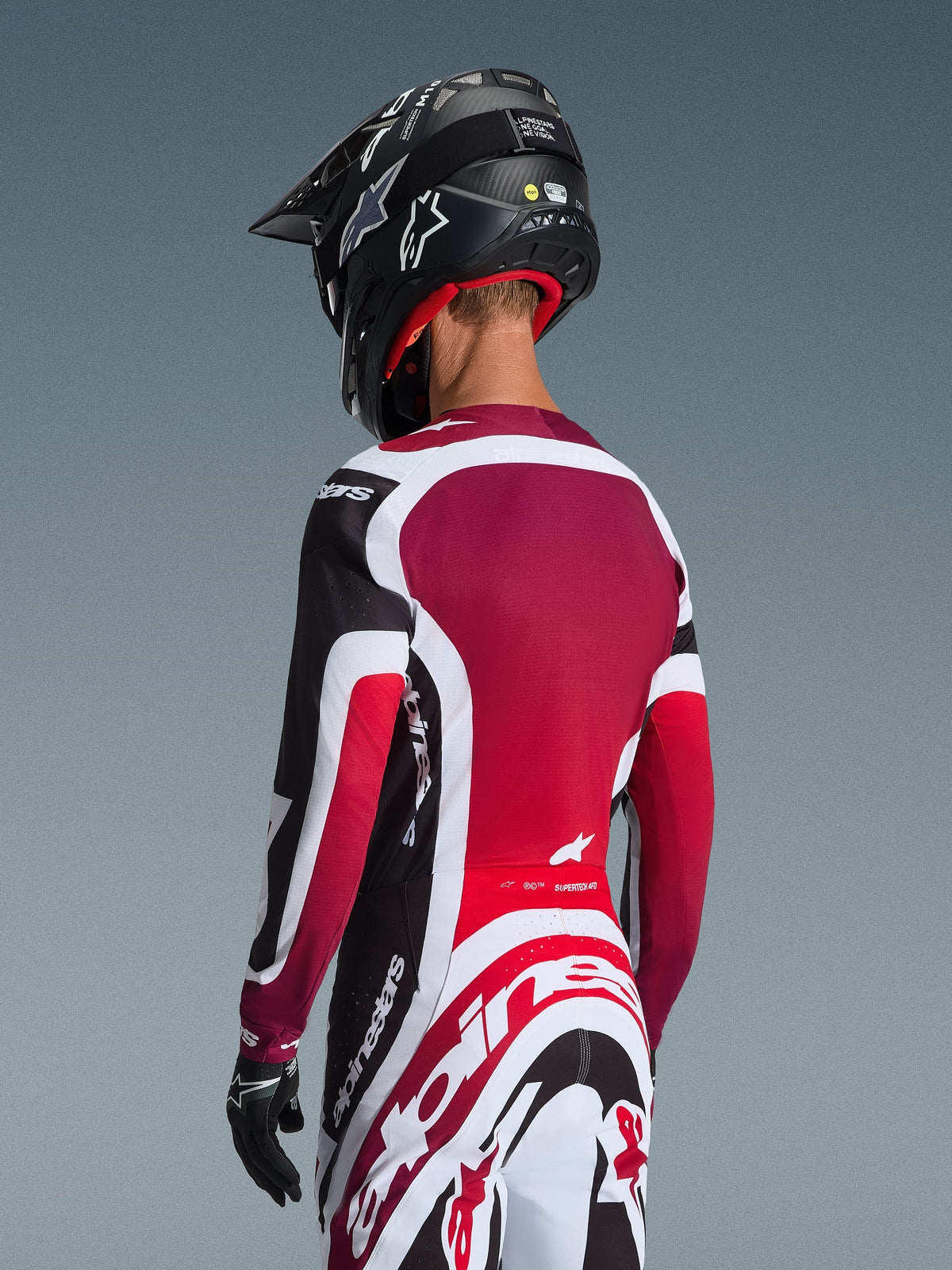 Set bagfra af en motocrosskører iført 2026 Supertech AFD Vista Jersey i sort, rød og hvid, koordineret med matchende bukser og en sort hjelm, med markant Alpinestars-branding, røde mesh-paneler og en atletisk racing-pasform.