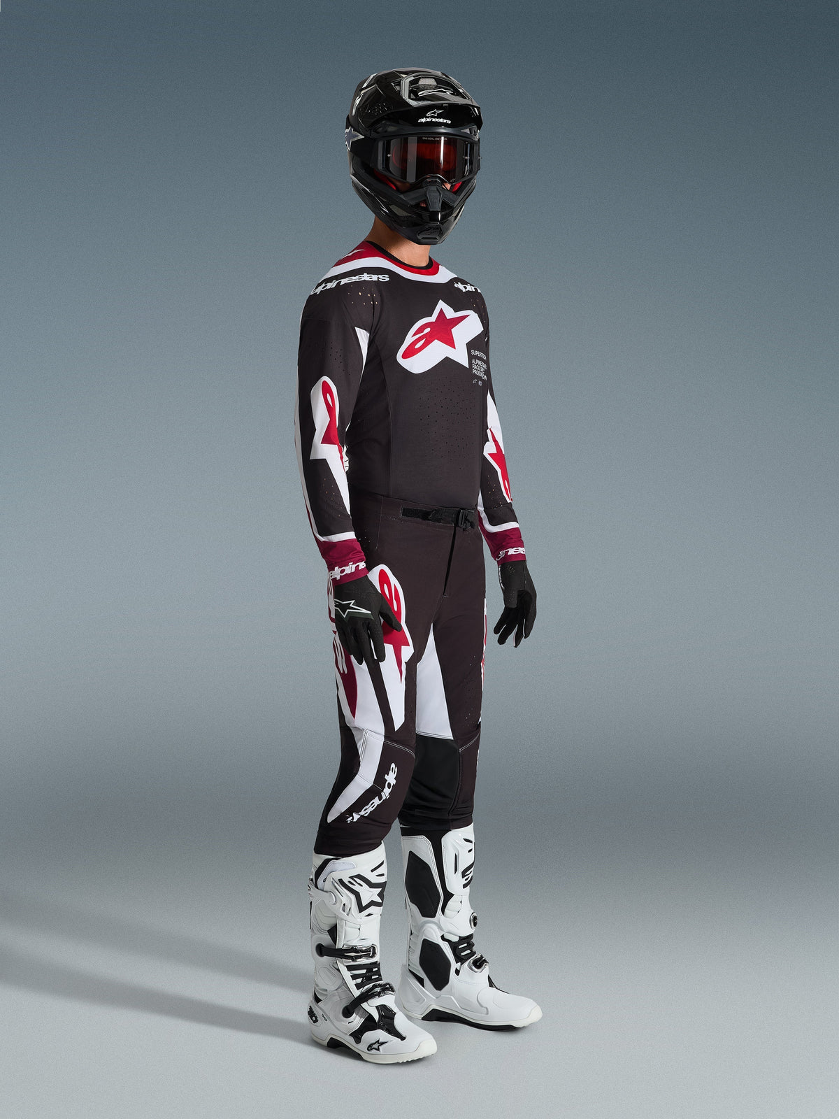 Motocrosskører iført komplet racerudstyr, 2026 Supertech AFD Vista-trøje i sort, rød og hvid, matchende motocrossbukser, sort hjelm med røde goggles, hvide og sorte støvler, sorte og hvide handsker, koordineret outfit til professionel off-road racing