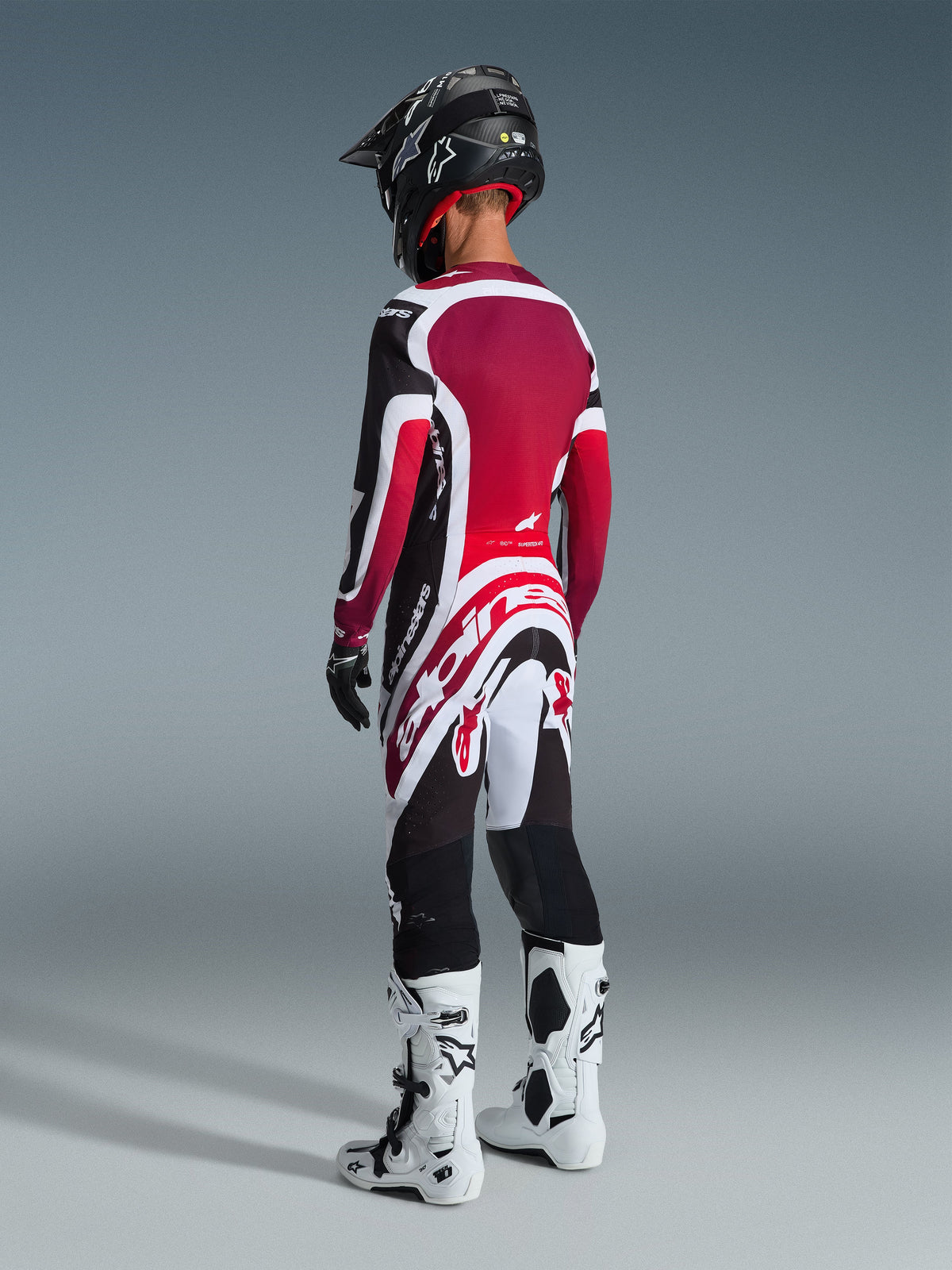Motocross rider viewed from behind wearing the Alpinestars 2026 Supertech AFD Vista Gear Set, Red White and Black jersey and pants with prominent Alpinestars branding, black helmet, white and black boots, and black gloves for a complete professional racing look.