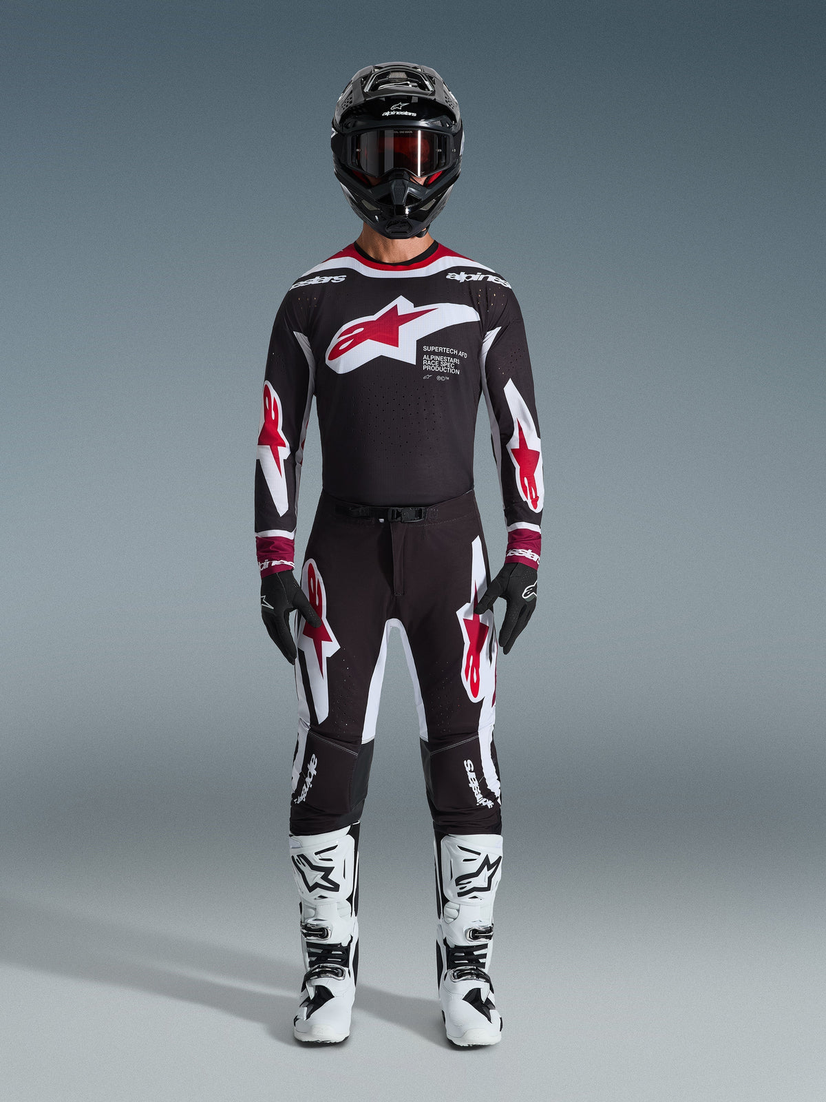 Motoc rosskøre r iført A lpinestar s 2026 Sup ertech AFD Vista-trø je, sort, rødt og hv idt racing -udstyr, m atchende s orte bukse r med røde stjernelog oer, hvide og sorte s tøvler, so rt hjelm m ed goggles , professi onelt off- road racin gsæt