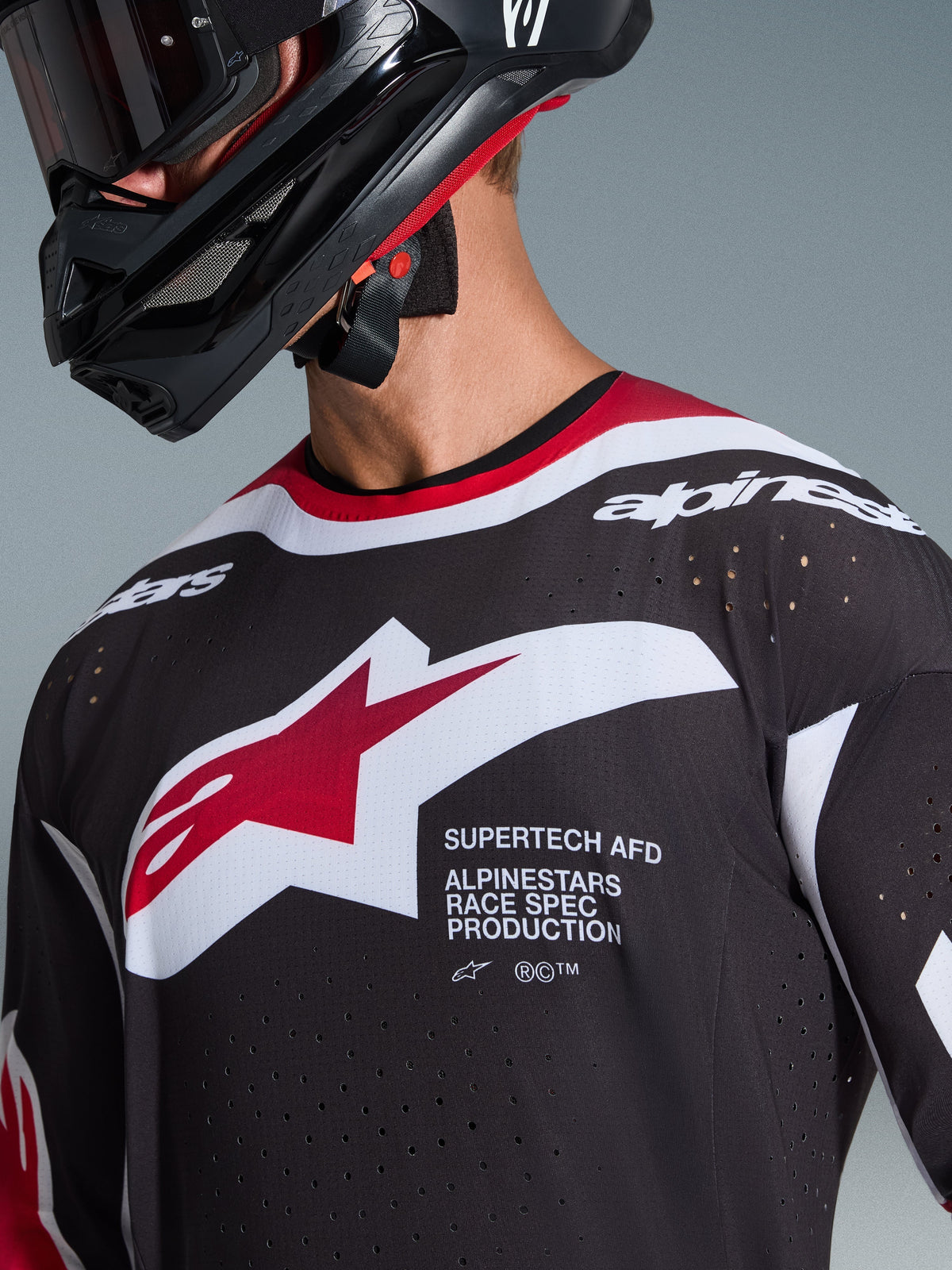 Alpinestars 2026 Supertech AFD Vista trøje, nærbillede af en motocrosskører iført en sort trøje med røde og hvide detaljer, med et stort hvidt og rødt Alpinestars-logo, laserskårne ventilationsperforeringer og professionel racing-pasform, kombineret med en sort hjelm.