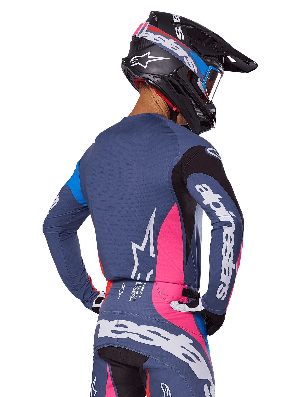 Motocross rider viewed from behind wearing the Alpinestars 2025 Techstar Dreem gear set in Gray, featuring a blue-gray jersey and pants with pink and black panels, white Alpinestars logos on the sleeves and back, and a matching black helmet with blue and pink graphics.