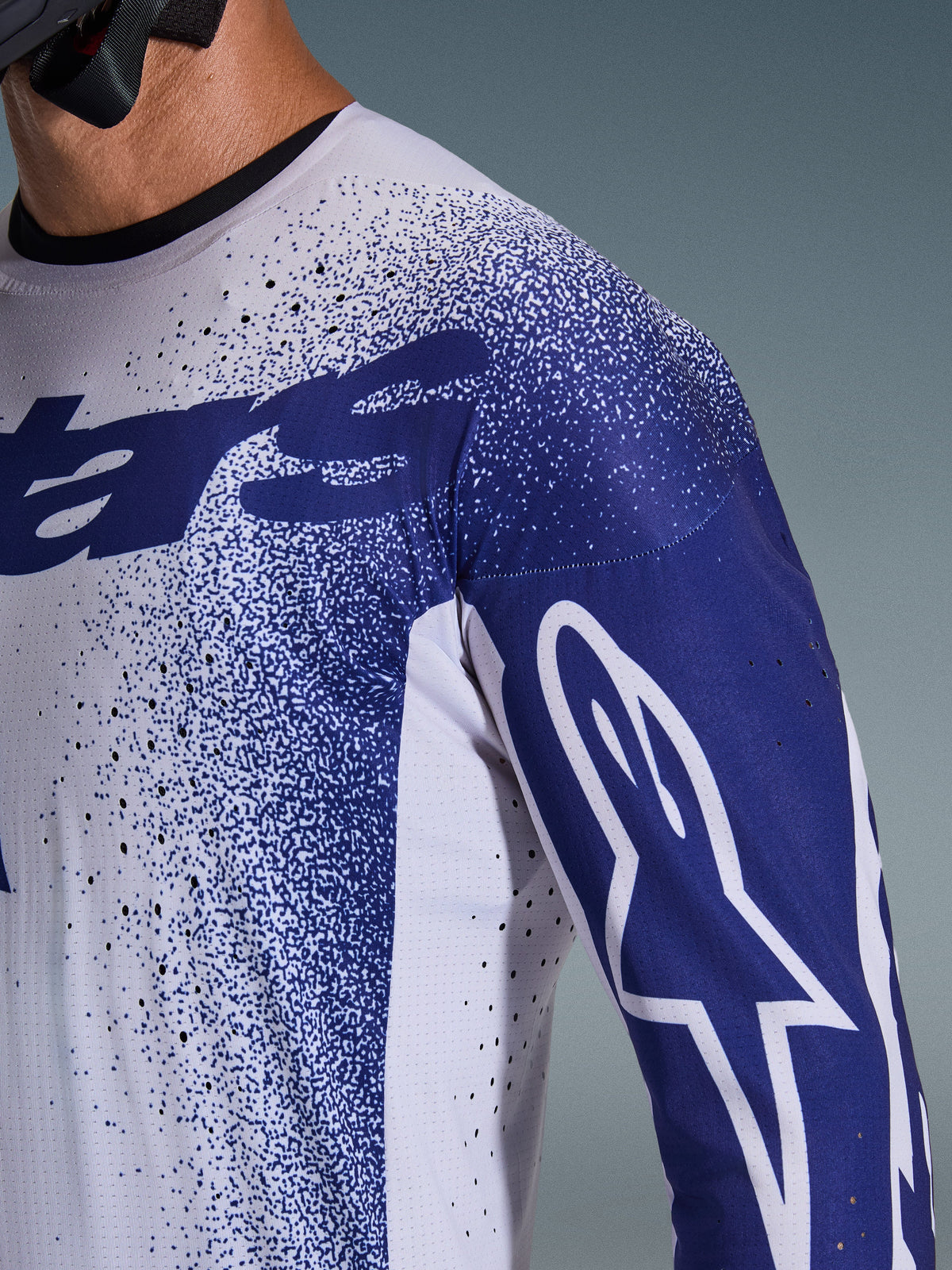 Alpinestars 2026 Supertech Scenz-trøje, lysegrå og mørkeblå, nærbillede af skulder og bryst med laserskårne perforeringer, hvidt Astars-logo på blåt ærme, nistret grafisk design, professionelt motocross-racerudstyr