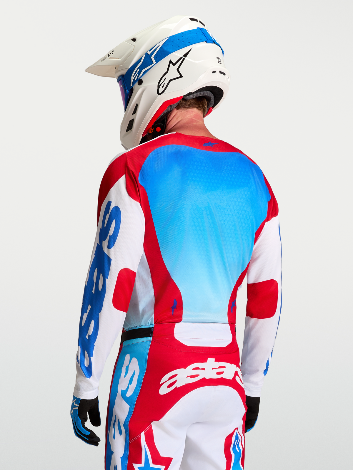 Alpinestars Racer Hunt motocrosstrøje, hvid, rød og blå, med meshpaneler og racepasform på en model set bagfra.