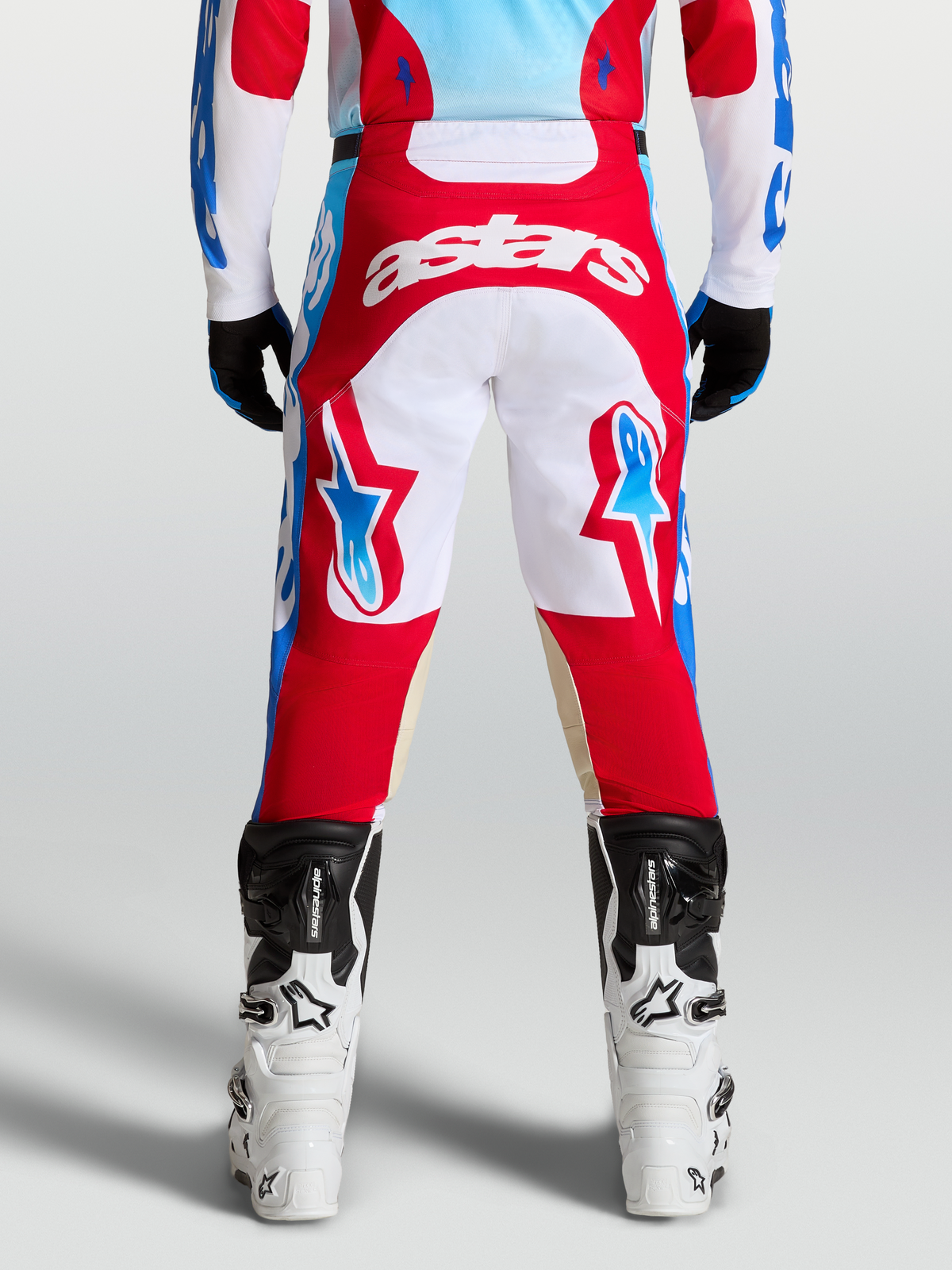 Alpinestars Racer Hunt Bukser, røde og hvide motocrossbukser set bagfra på en rytter, med lyseblå detaljer og ergonomisk forbuet benkonstruktion.