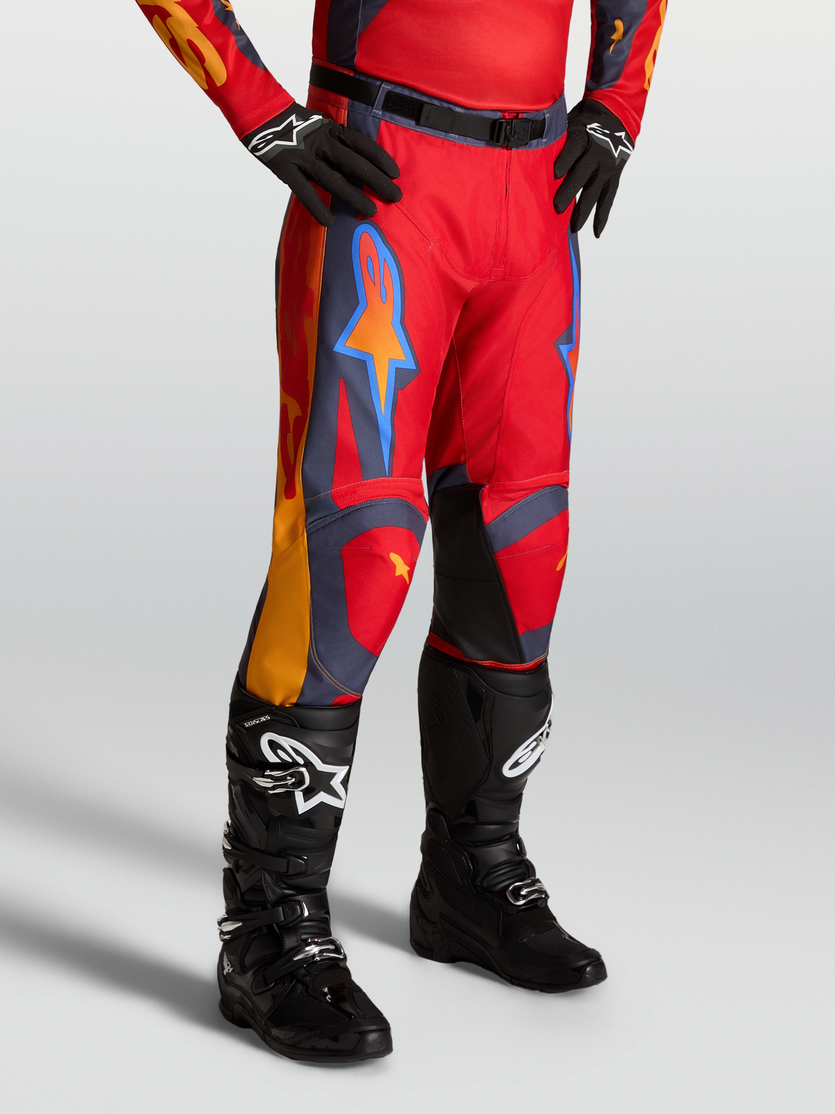 Alpinestars Racer Hunt bukser, rød motocrossbukser til mænd med grå og orange detaljer, vist på model med sorte støvler.