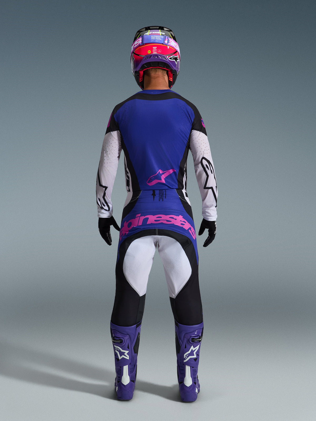 Motocrosskører set bagfra iført 2026 Techstar Knif trøje, sort, lysegrå og lilla, matchende motocrossbukser med lyserødt branding, lilla støvler og hjelm, koordineret high-performance off-road udstyr