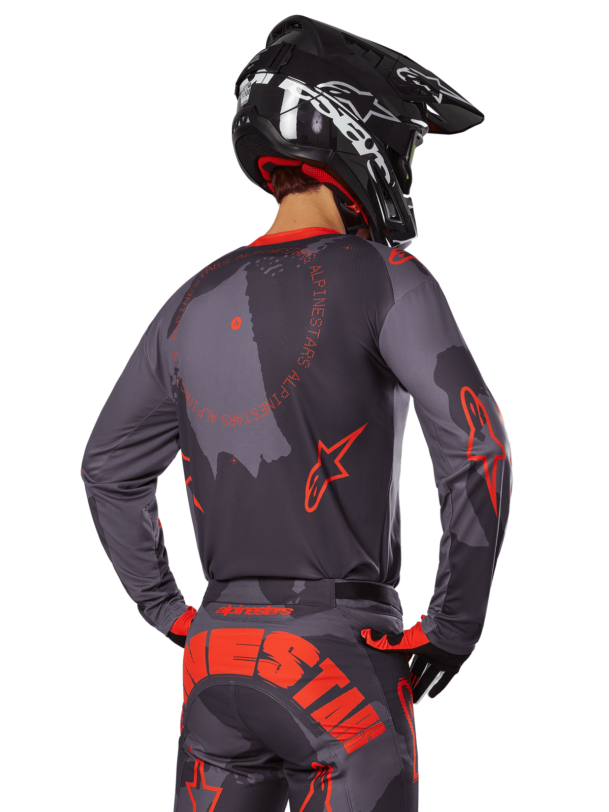 Alpinestars 2025 Racer Hollow trøje, set bagfra af en motocross-kører i Gray Camo og Orange Fluo udstyr, med matchende camo-bukser med stor orange Alpinestars-skrift og en sort hjelm, professionelt design til terrænkørsel