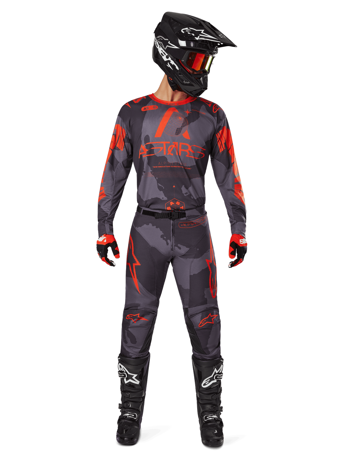 Motocrosskører iført Alpinestars 2025 Racer Hollow-trøje og matchende bukser i Gray Camo Orange Fluo, komplet udstyrssæt med sort hjelm, briller, handsker og støvler, med markante orange logoer og camouflage-mønster.