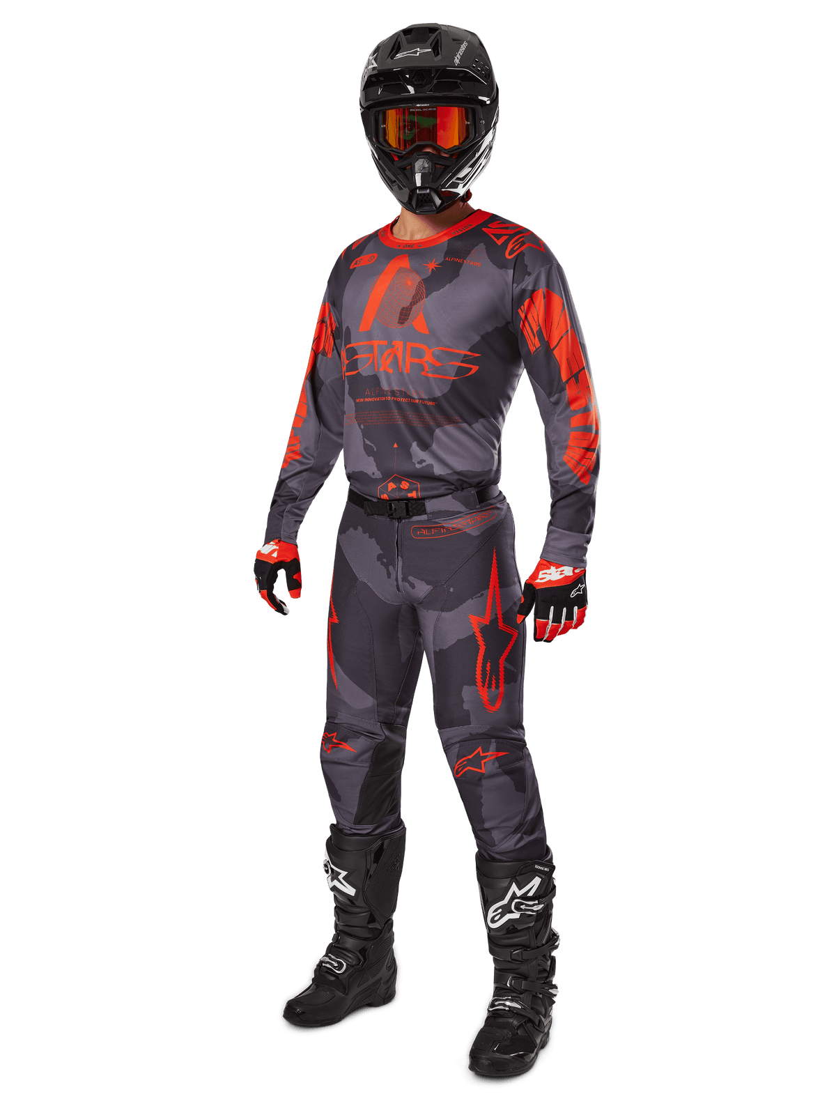 Motocross-kører i komplet racerudstyr, Alpinestars 2025 Racer Hollow trøje og bukser i Gray Camo Orange Fluo, sort hjelm med orange briller, sorte og røde handsker og sorte støvler med hvide logoer, koordineret præstationsoutfit til off-road kørsel