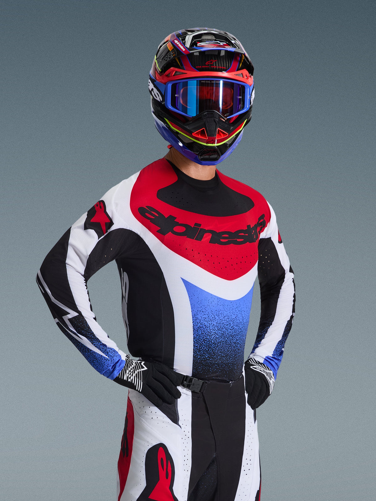 Alpinestars 2026 Techstar Knif udstyrssæt, motocross-kører i rød, hvid og blå racing-jersey med sorte detaljer, matchende flerfarvet hjelm og briller, sorte handsker, professionelt udstyr til motocross-konkurrence.