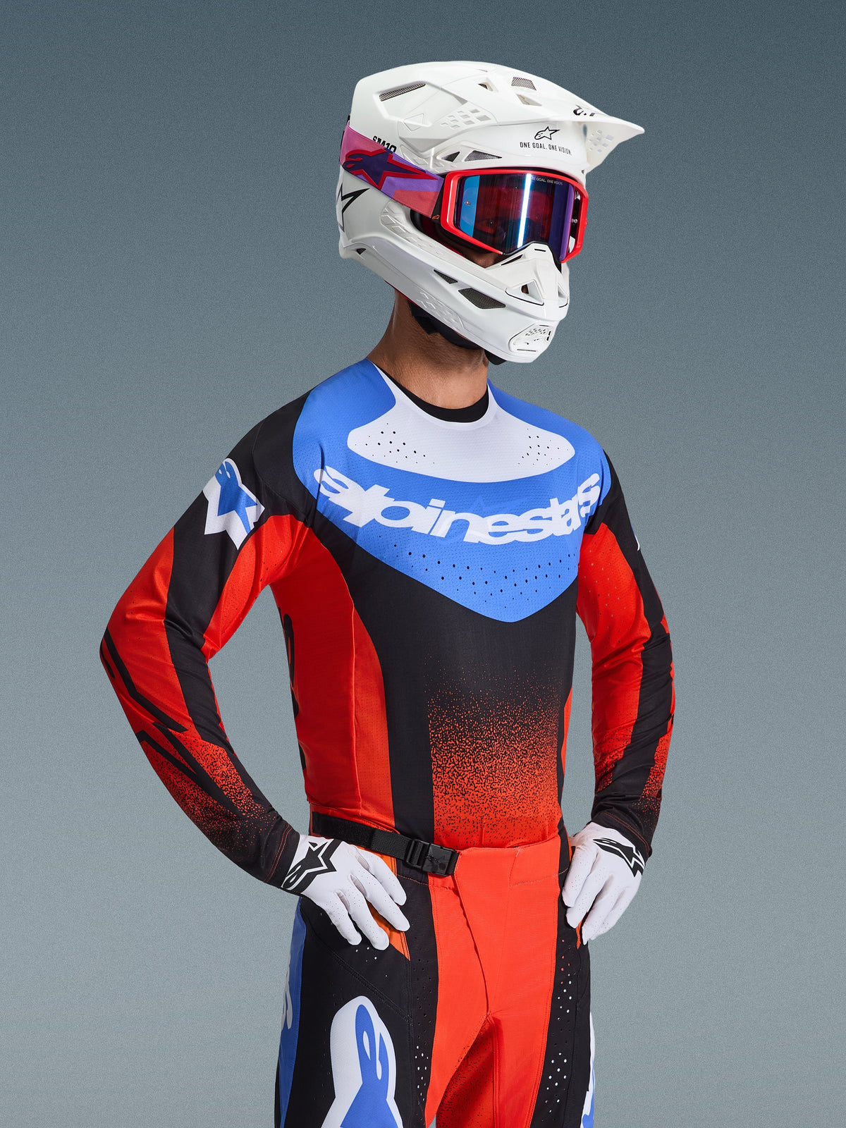 Motocrosskører iført Alpinestars 2026 Techstar Knif-udstyrssæt, blå jersey med hvidt logo og røde ærmer, matchende sorte og røde bukser med blå detaljer, hvid hjelm med røde goggles, hvide og sorte handsker, professionelt raceroutfit til motocross