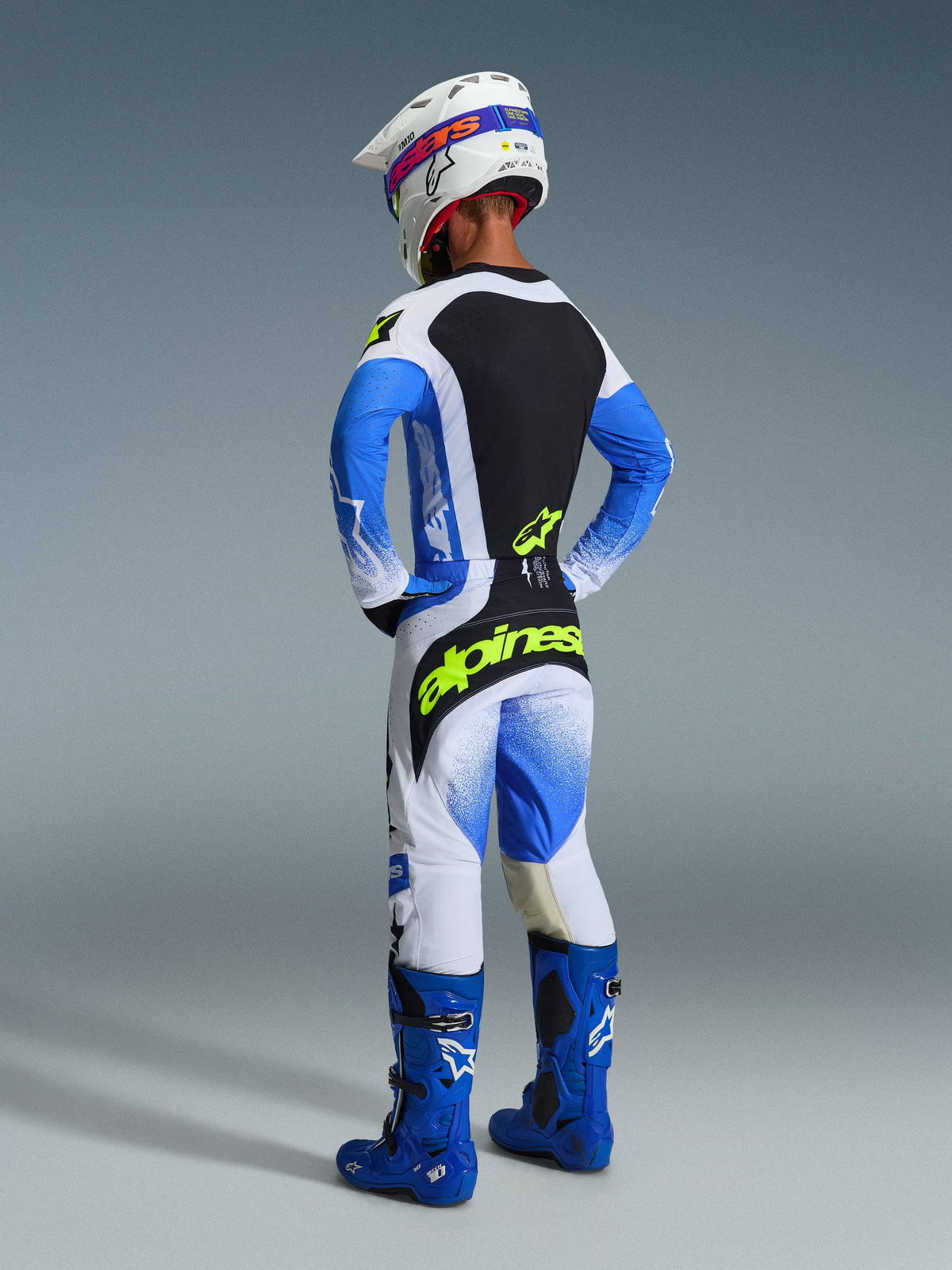 Motocrosskører set bagfra iført det komplette Alpinestars 2026 Techstar Knif-udstyrssæt i Ucla Blue og sort, med en jersey med sort rygpanel og gult fluo-logo, matchende blå og hvide bukser med markant gul branding, blå motocross-støvler og en hvid racerhjelm.