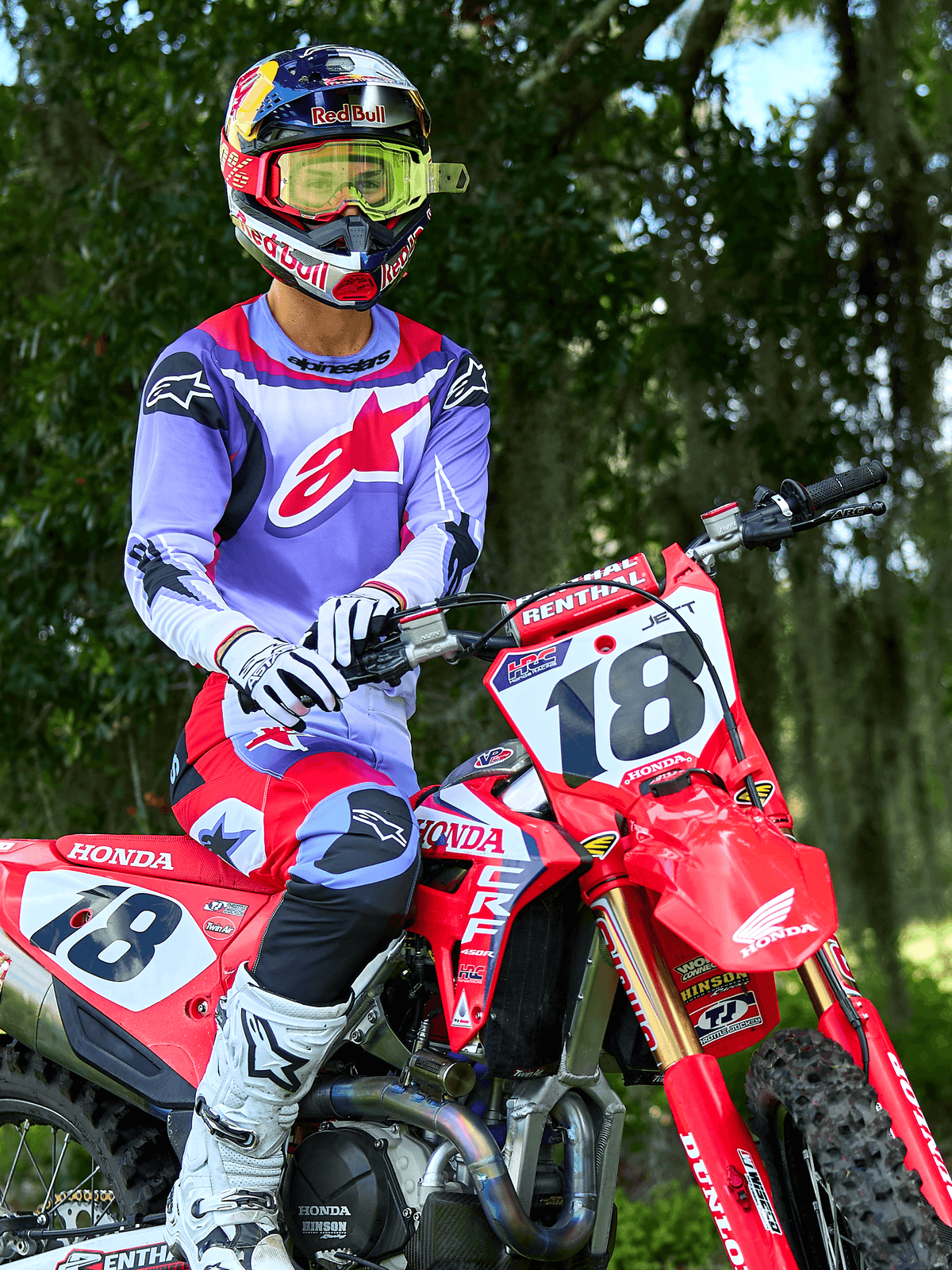 Motocross-kører på en rød Honda CRF-crosser, iført Alpinestars 2025 Fluid Wurx-trøje i lilla og klar rød, matchende lilla og røde bukser, Red Bull-hjelm med gule goggles, hvide Alpinestars-støvler og -handsker, professionelt MX-udstyr til off-road-kørsel