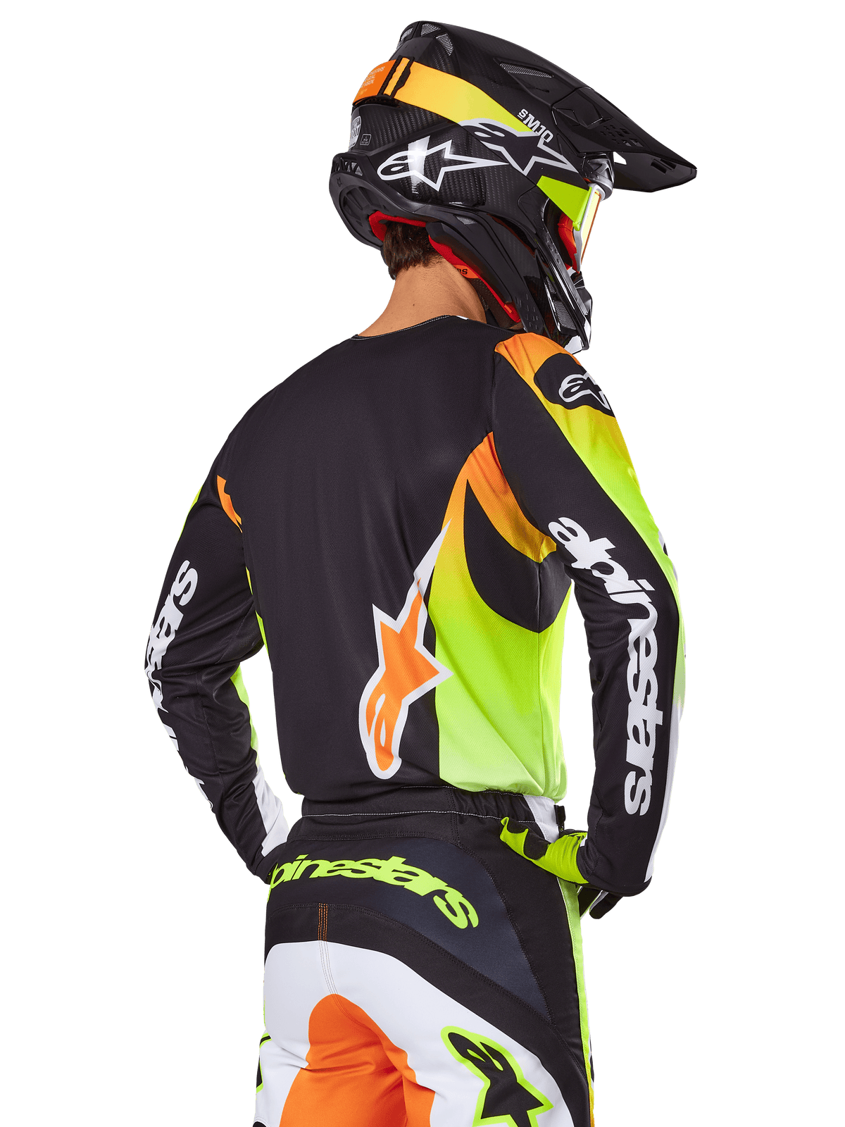 Motocrosskører set bagfra iført Alpinestars 2025 Fluid Wurx-udstyrssæt, sort trøje med neongul og orange grafik, matchende bukser med hvide og orange paneler, sort hjelm med neon-detaljer, tydelig Alpinestars-branding på ærmer og bagpå