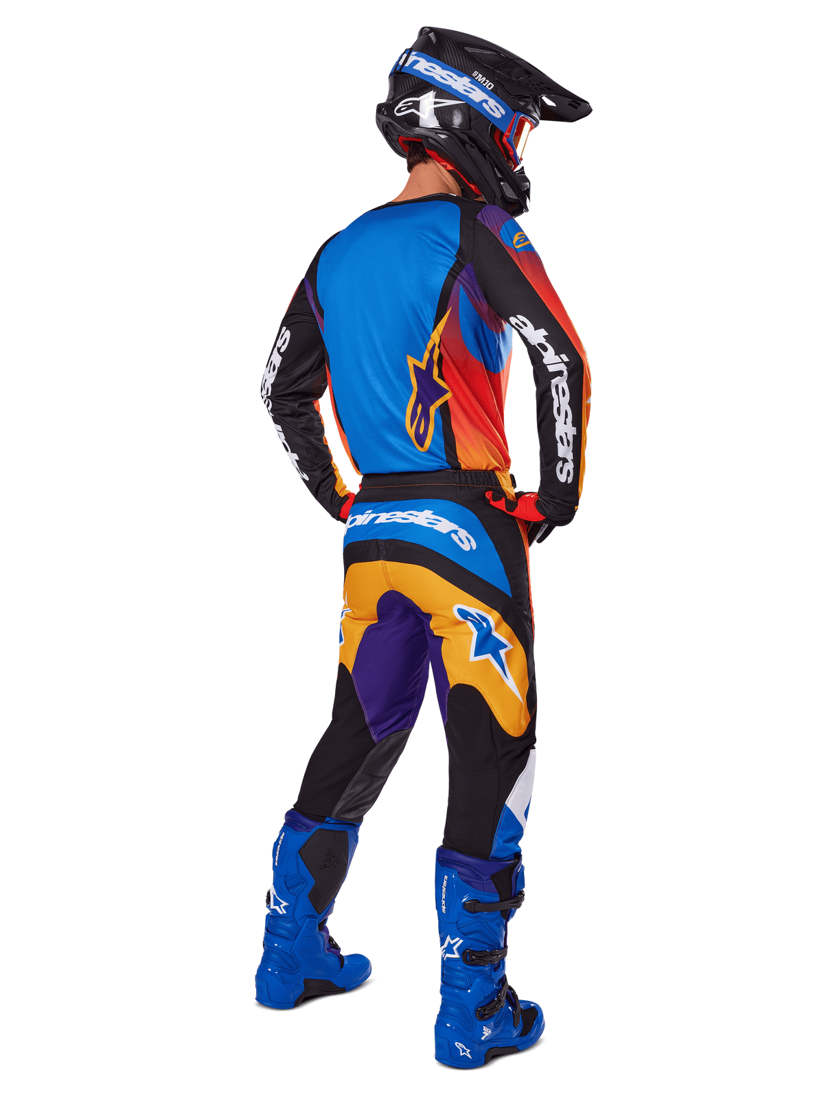 Motocross-rytter set bagfra iført Alpinestars 2025 Fluid Wurx-udstyrssæt, flerfarvet trøje med blå, orange og lilla paneler, matchende bukser med hvidt Alpinestars-logo på sædet, klare blå støvler og en sort hjelm, koordineret outfit til off-road racing