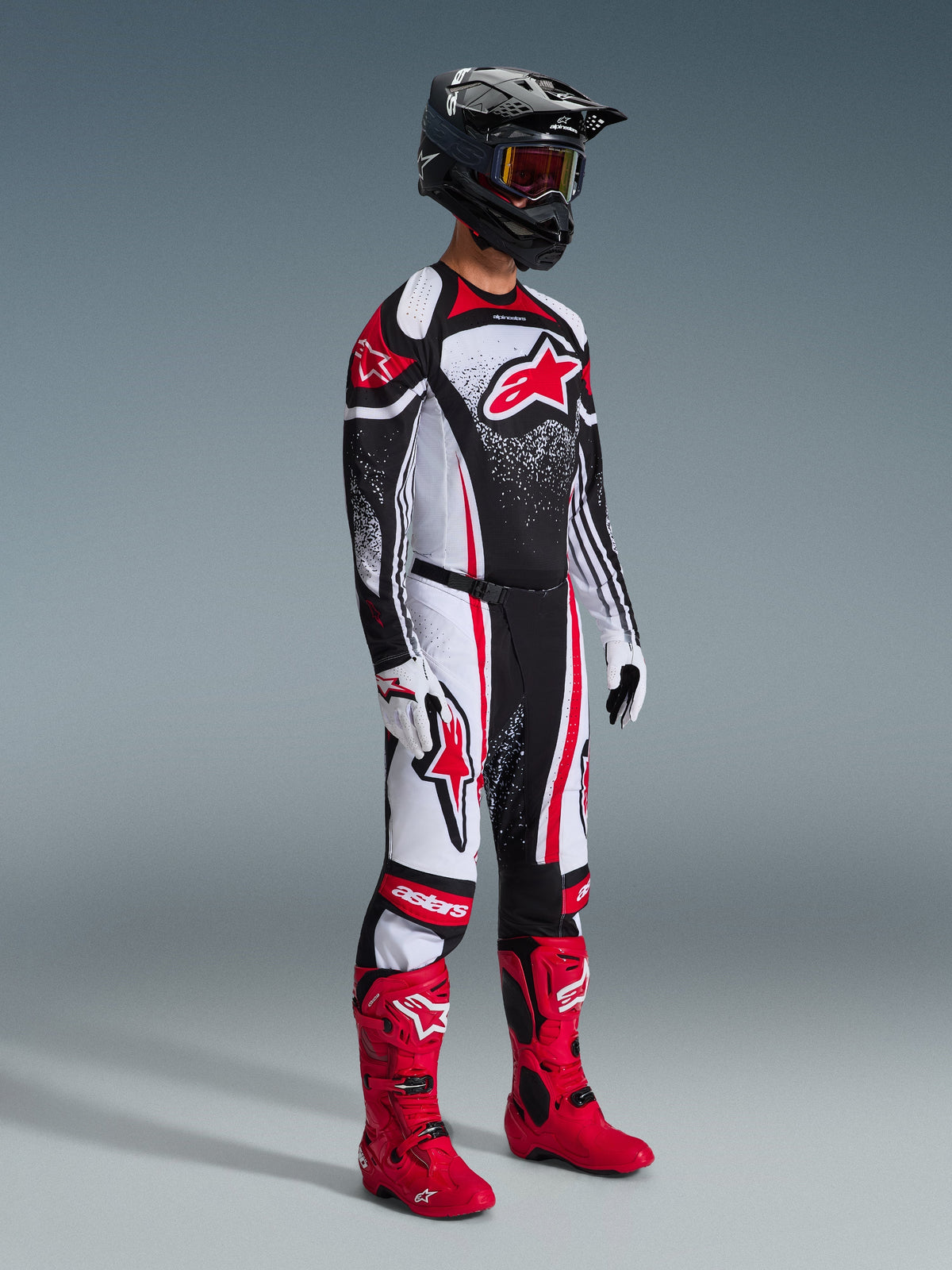 Alpinestars 2026 Techstar Nomur jersey, motocross-kører iført sort, hvidt og rødt racerudstyr, matchende bukser med røde detaljer, sort hjelm, klare røde støvler og hvid-sorte handsker, komplet professionelt motocross-udstyr til terrænkørsel.