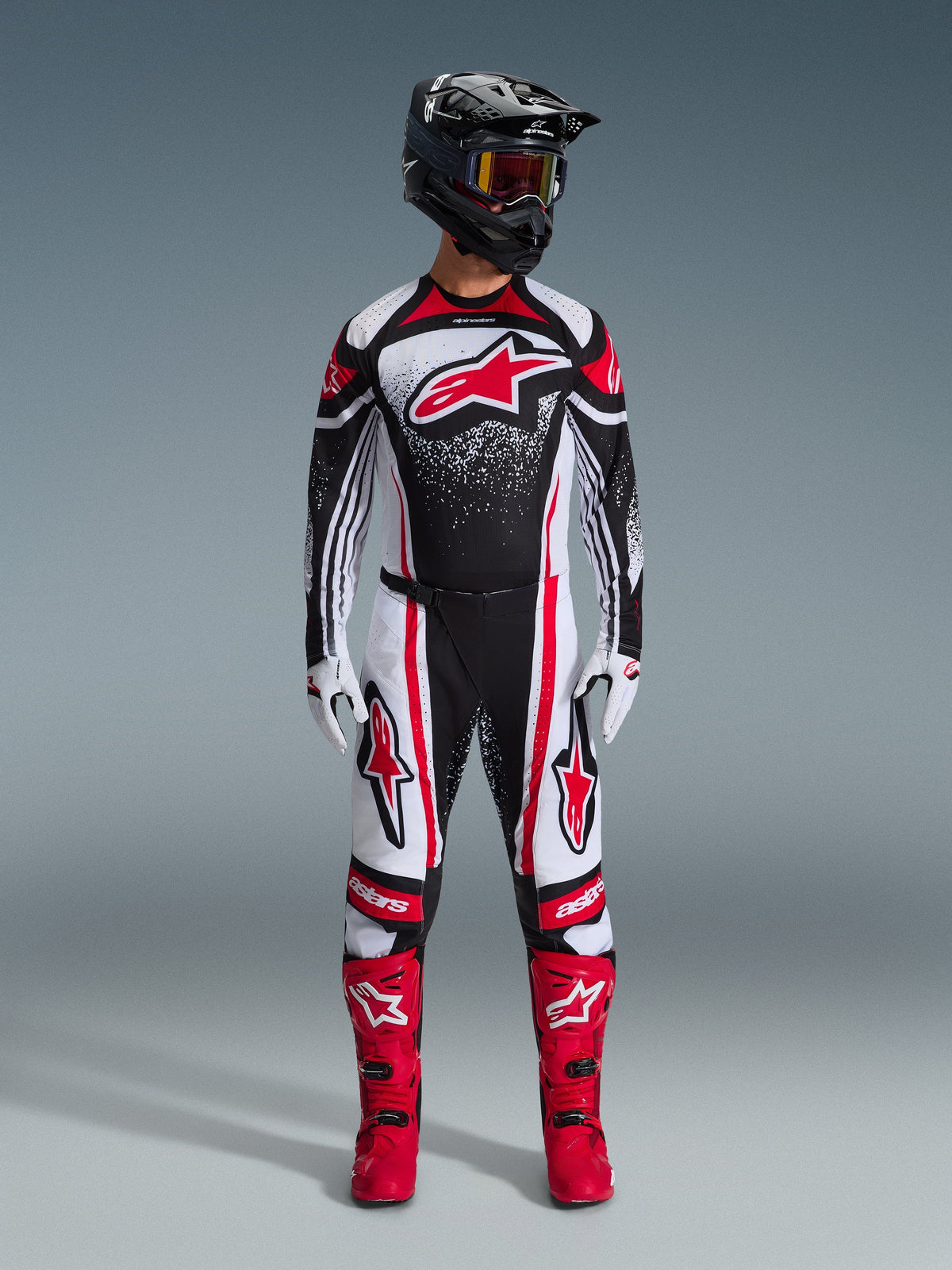 Motocross-kører iført fuldt Alpinestars-racerudstyr, 2026 Techstar Nomur Jersey i Black White Red, matchende bukser med røde detaljer, sort hjelm og klare røde støvler, stort rødt Astars-logo på brystet med spættet gradientmønster, koordineret outfit til off-road-konkurrence
