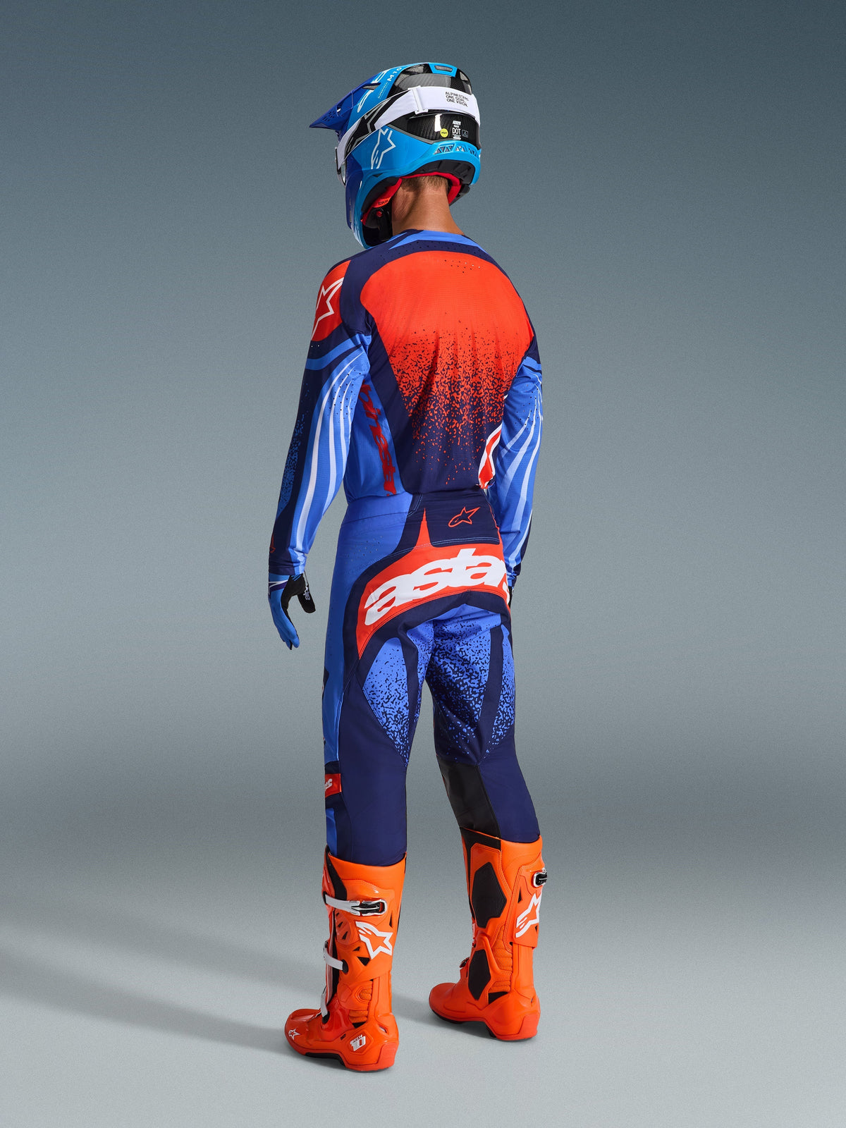 Motocrosskører set bagfra iført 2026 Techstar Nomur-udstyrssættet, mørkeblå og UCLA-blå trøje med orange panel, matchende bukser med orange 'astars'-logo, lyseorange motocross-støvler og en blå og hvid hjelm, koordineret racerudstyr til konkurrence