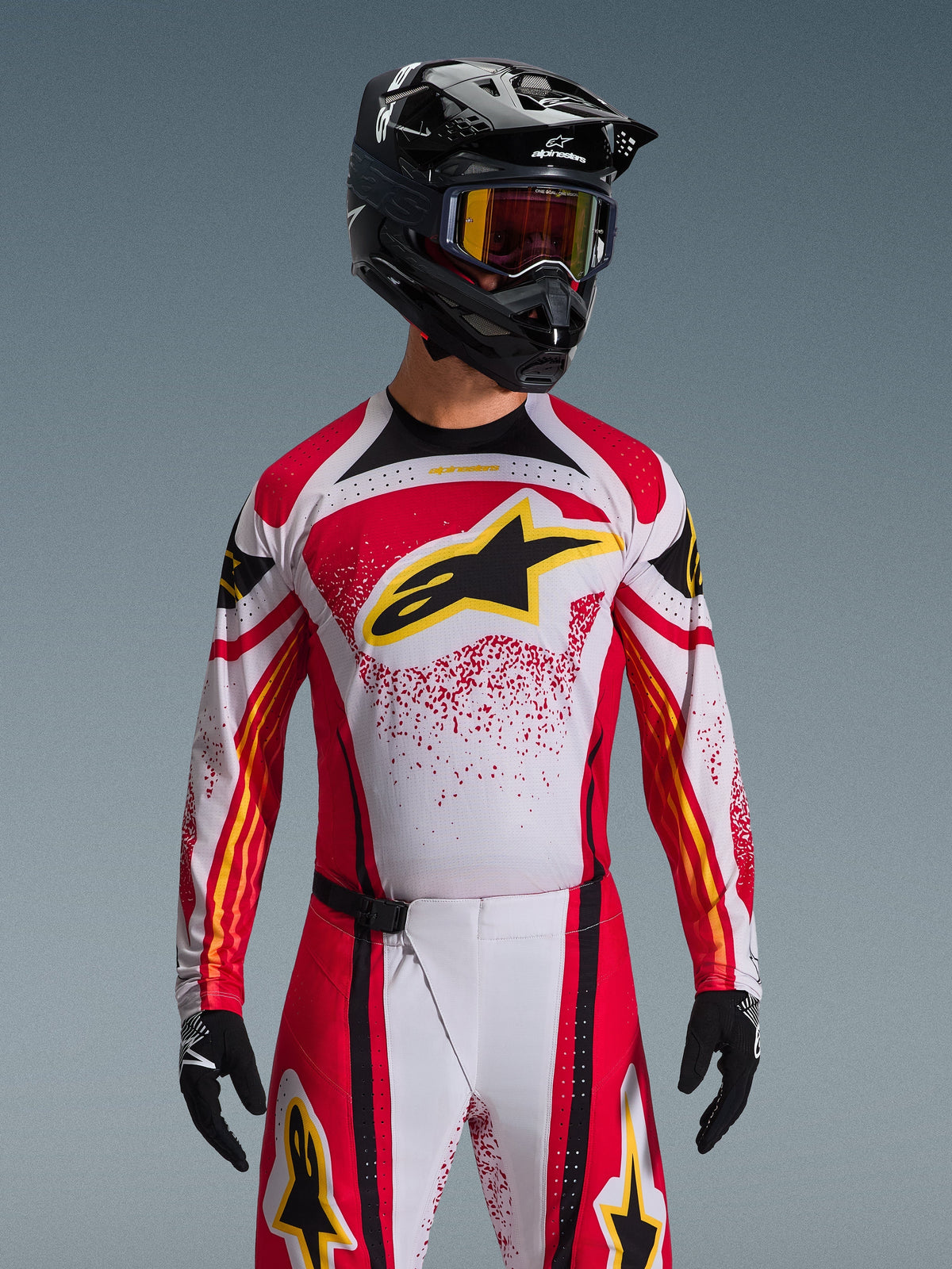 Alpinestars 2026 Techstar Nomur trøje, motocross-trøje, rød, hvid og sort, med et stort sort A-star-logo på brystet med gule detaljer, rødt splatter-design, vist med en sort hjelm og matchende off-road-udstyr