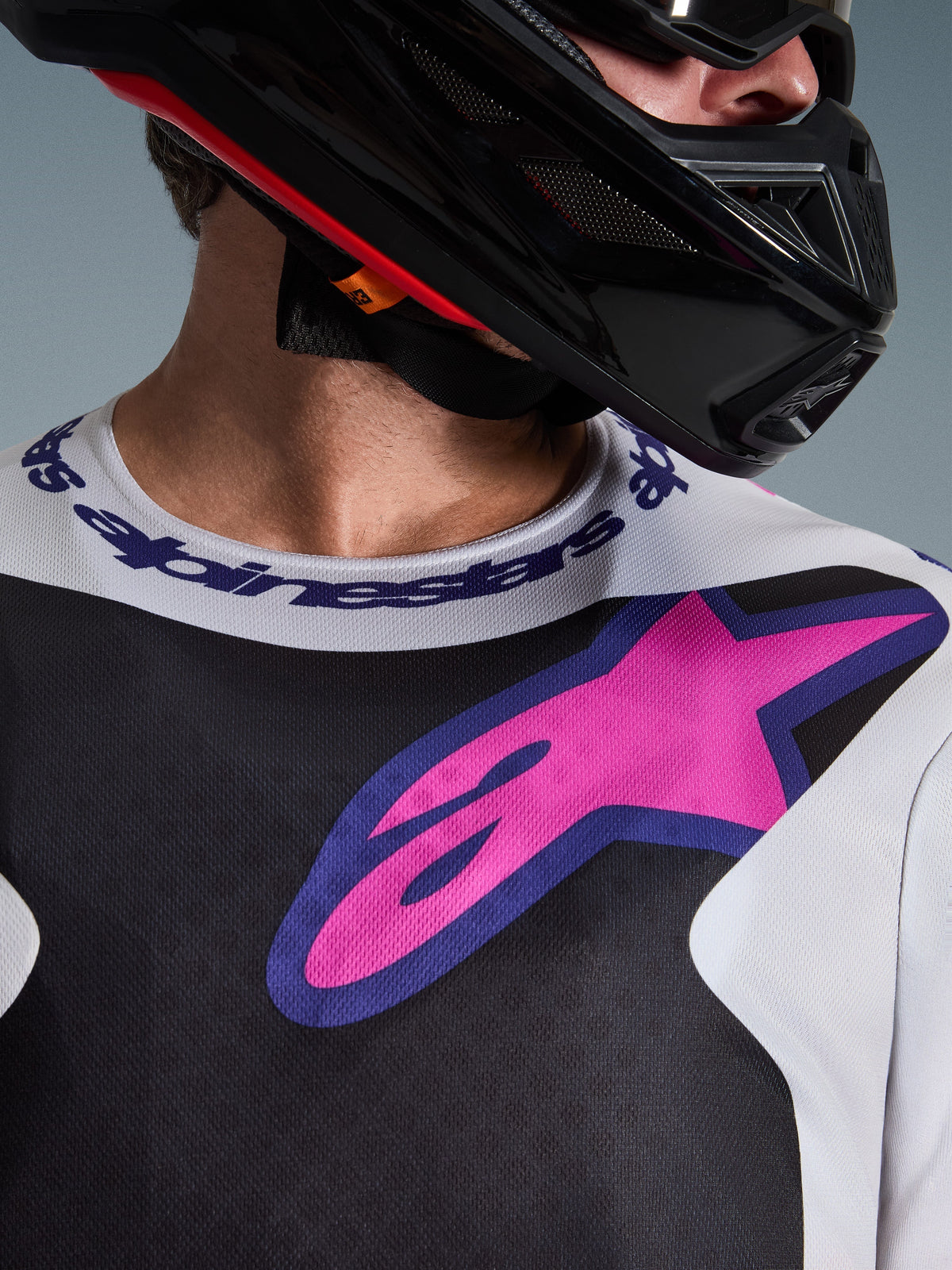 Alpinestars 2026 Fluid Grid trøje, motocross-trøje, sort, lysegrå og lilla, nærbillede af bryst- og halsområde med stort pink stjernelogo, sportskrave med branding, båret med sort hjelm, performance off-road-udstyr